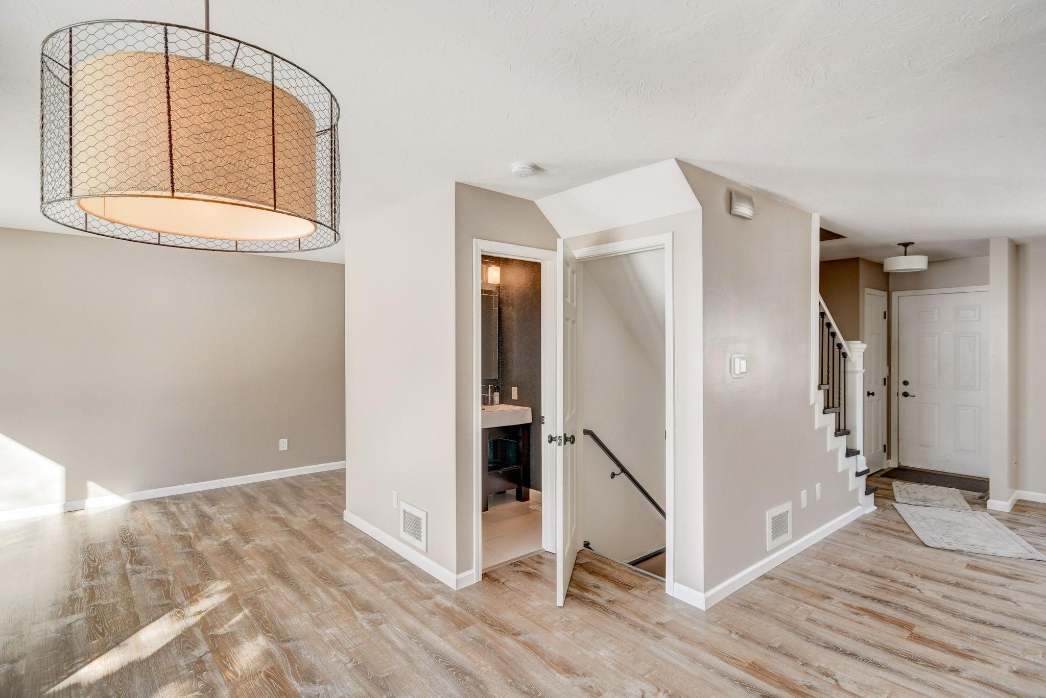 Entryway with a wire-cage pendant, staircase, front door, and doors to a bathroom and lower-level stairs.
