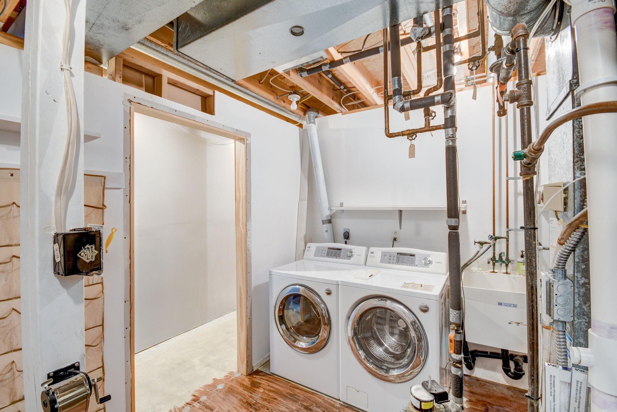Laundry area with front-loading washer and dryer beside a utility sink and exposed plumbing.