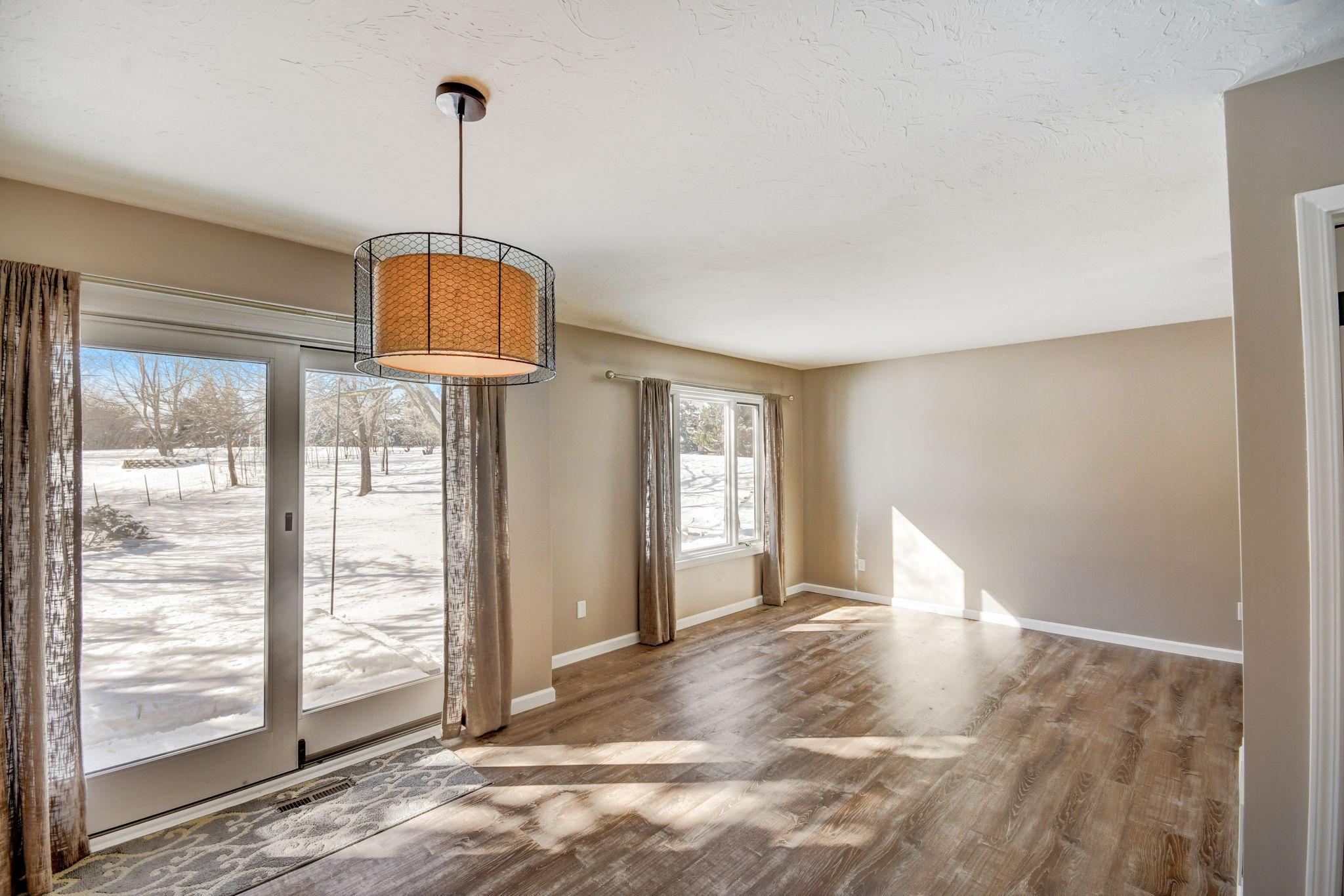 Empty dining area with a drum pendant light, wood-look floors, and sliding glass doors overlooking snow.