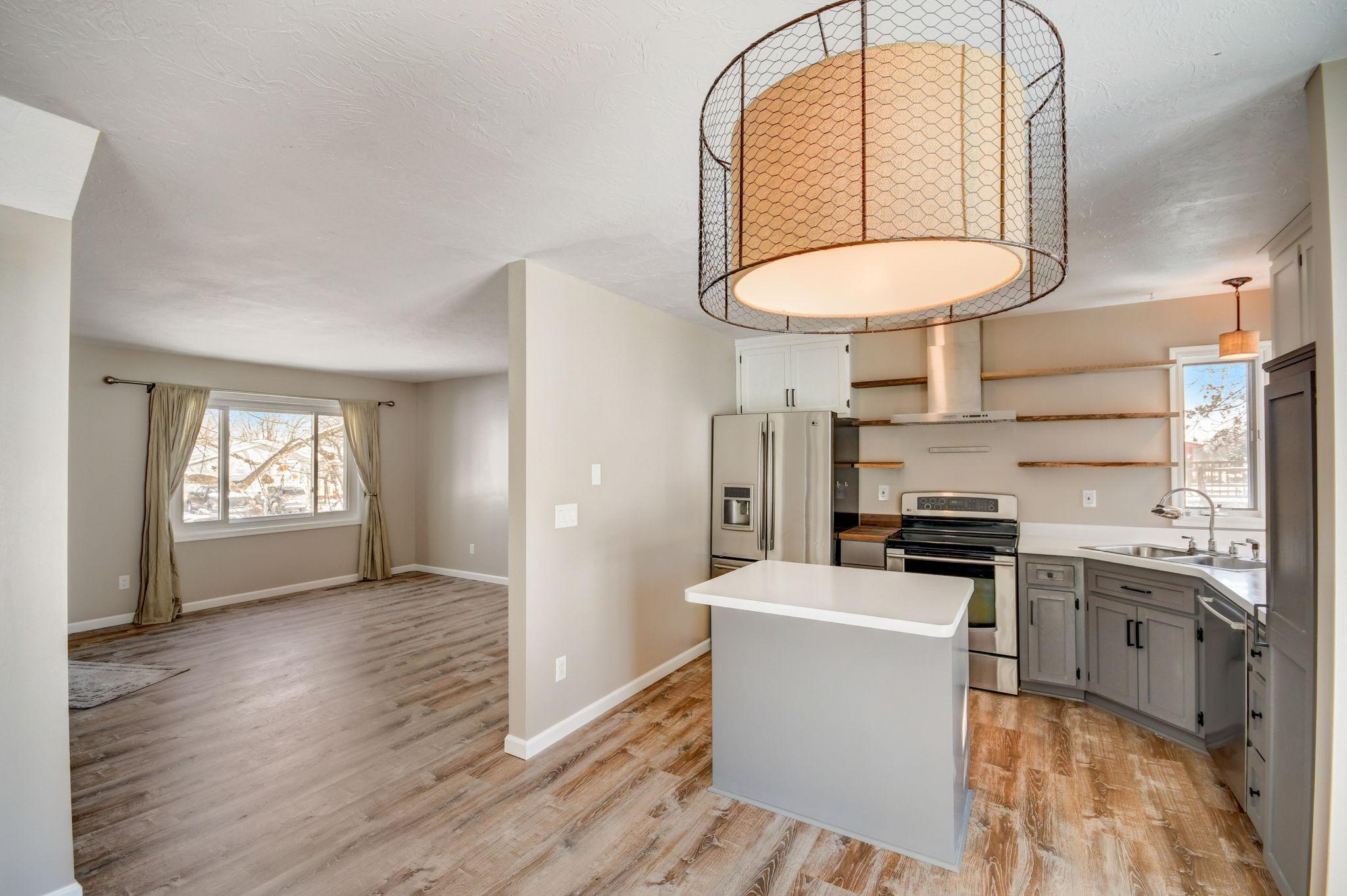 Open kitchen with gray cabinets, stainless appliances, white island, and adjoining living area.
