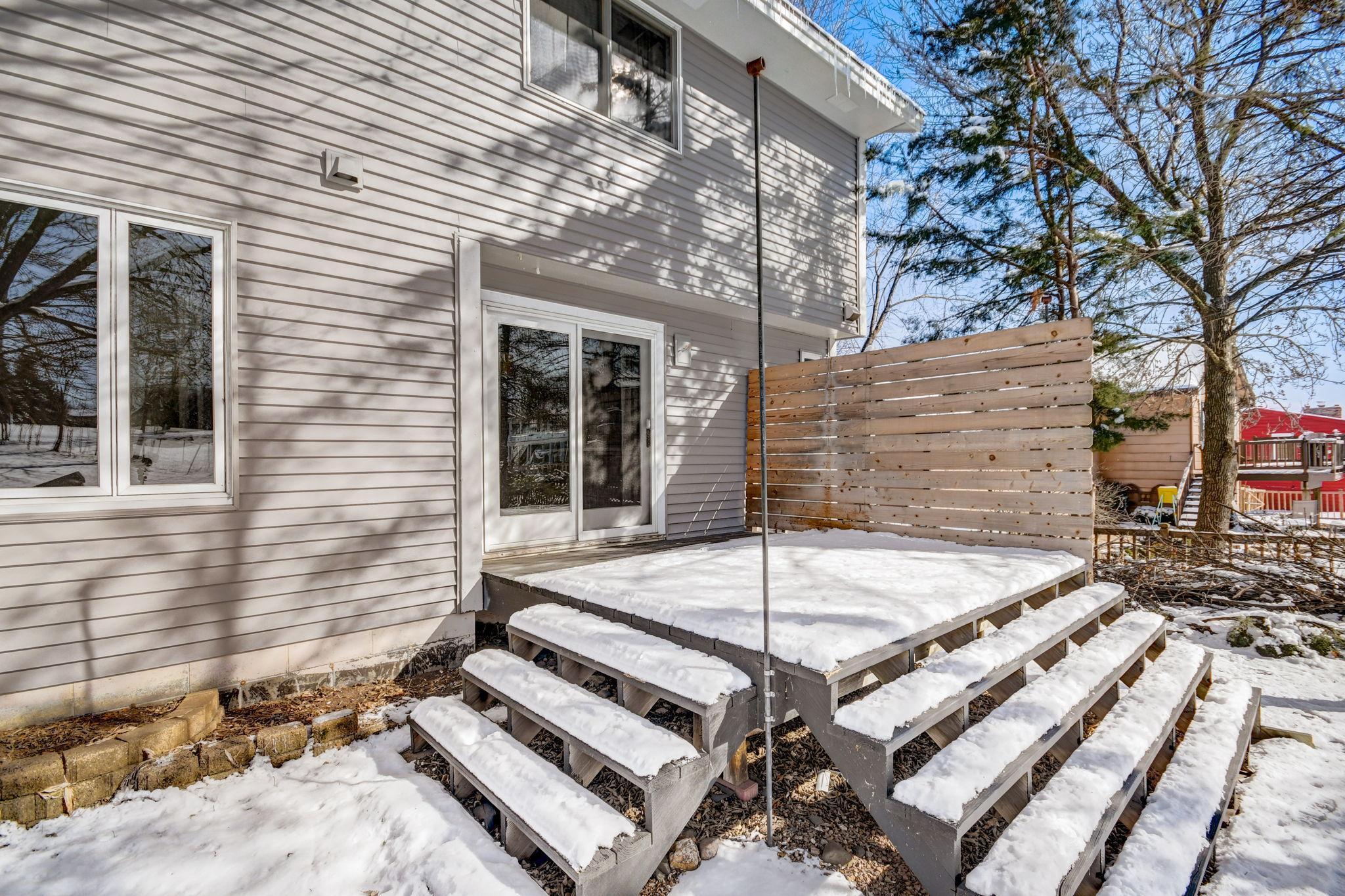 House exterior with a snow-covered raised deck, wooden privacy screen, and tiered steps.