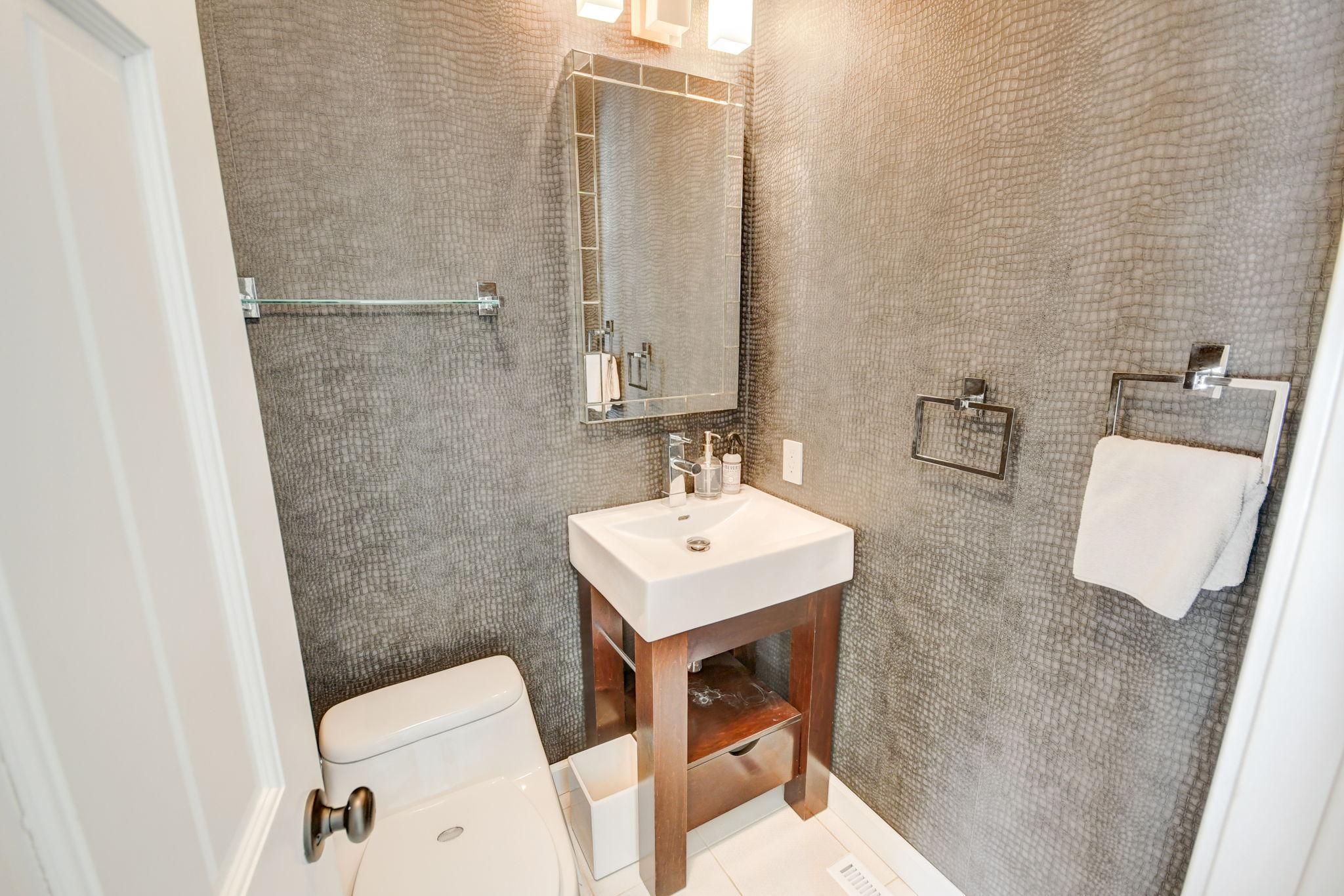 Bathroom with textured gray tile, a white sink on a wooden vanity, and a toilet.