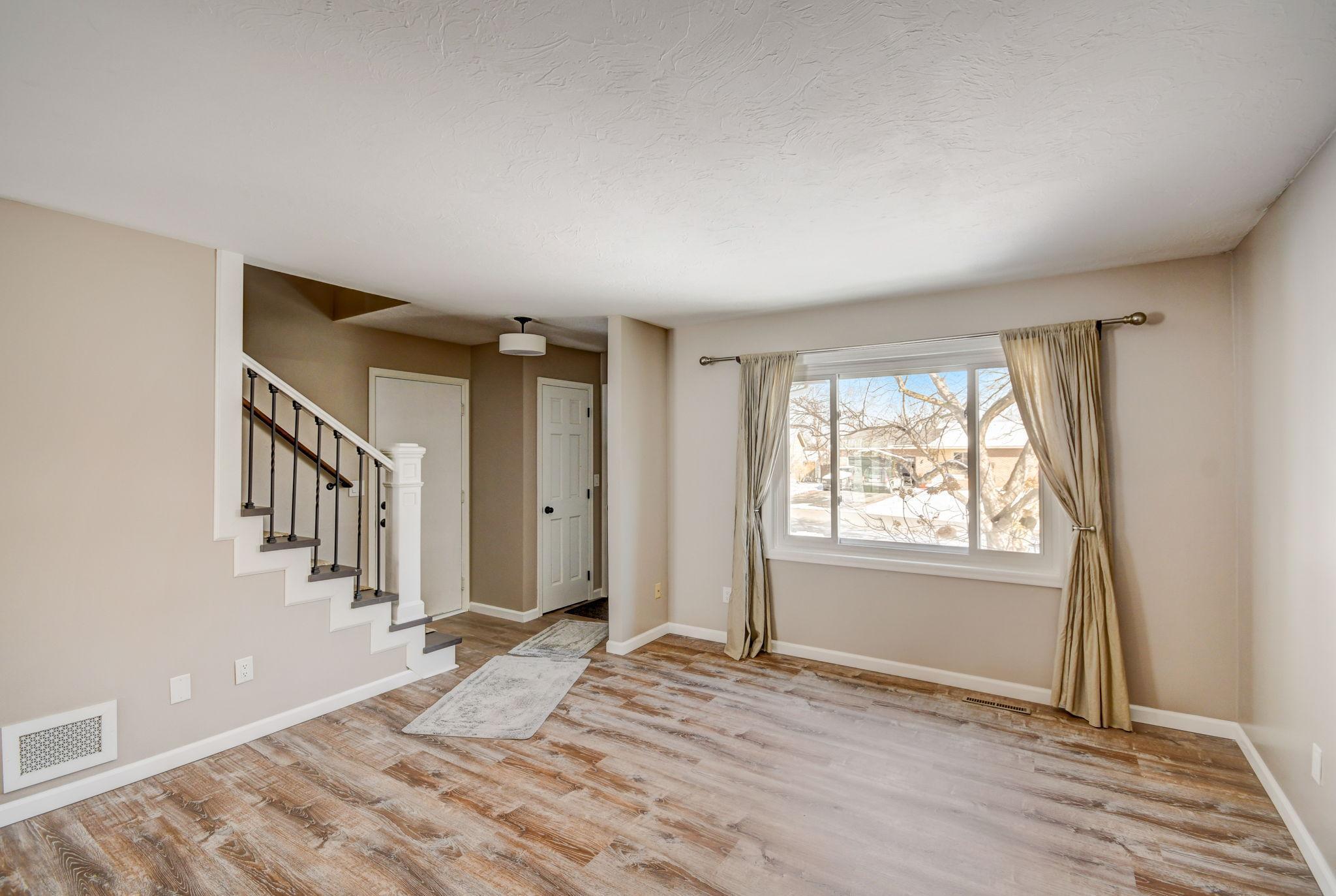 Unfurnished living room with a staircase, wood-look flooring, and a large window overlooking snow.