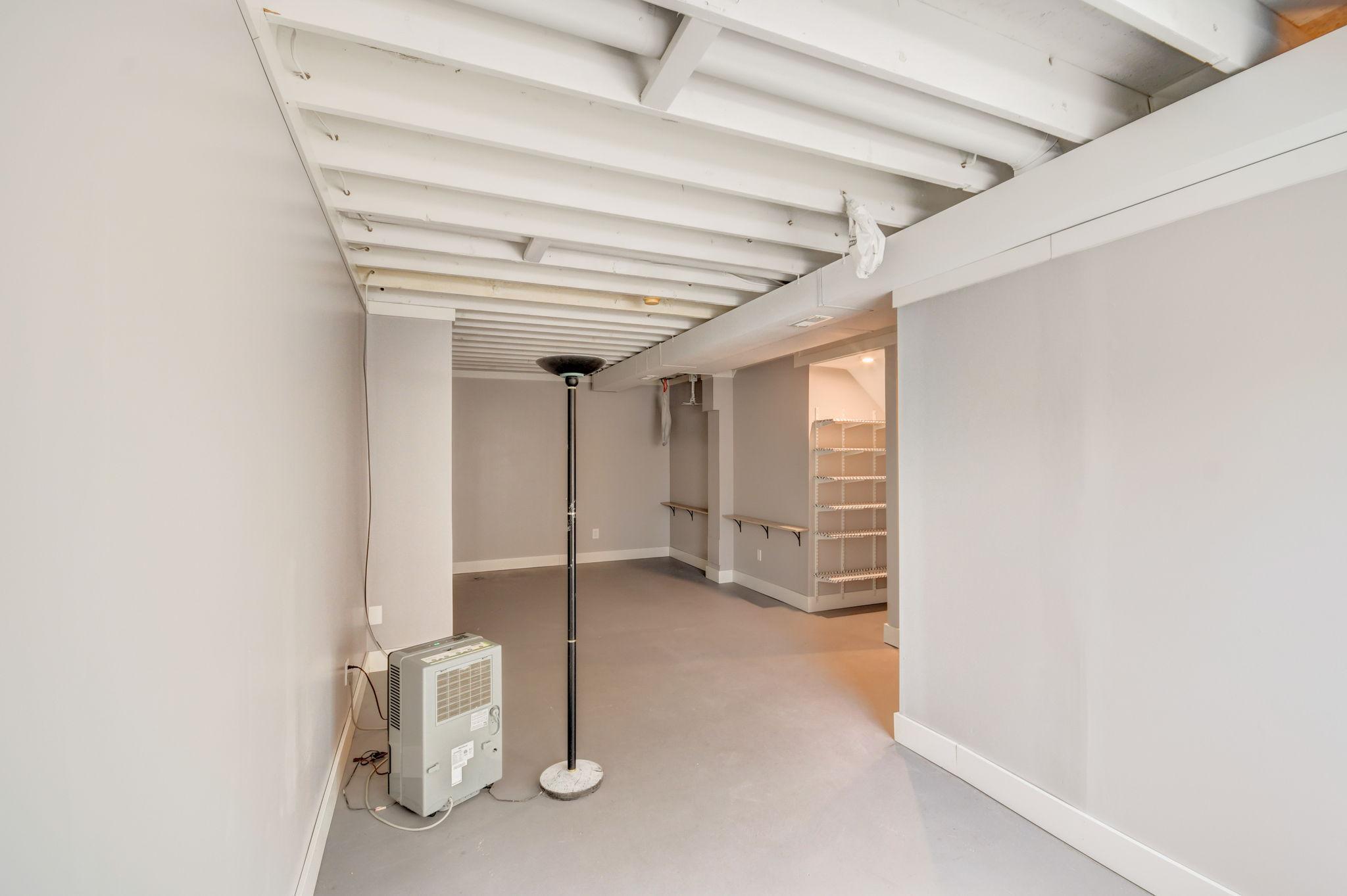 Basement room with exposed ceiling joists, gray flooring, wall shelves, and a portable dehumidifier.