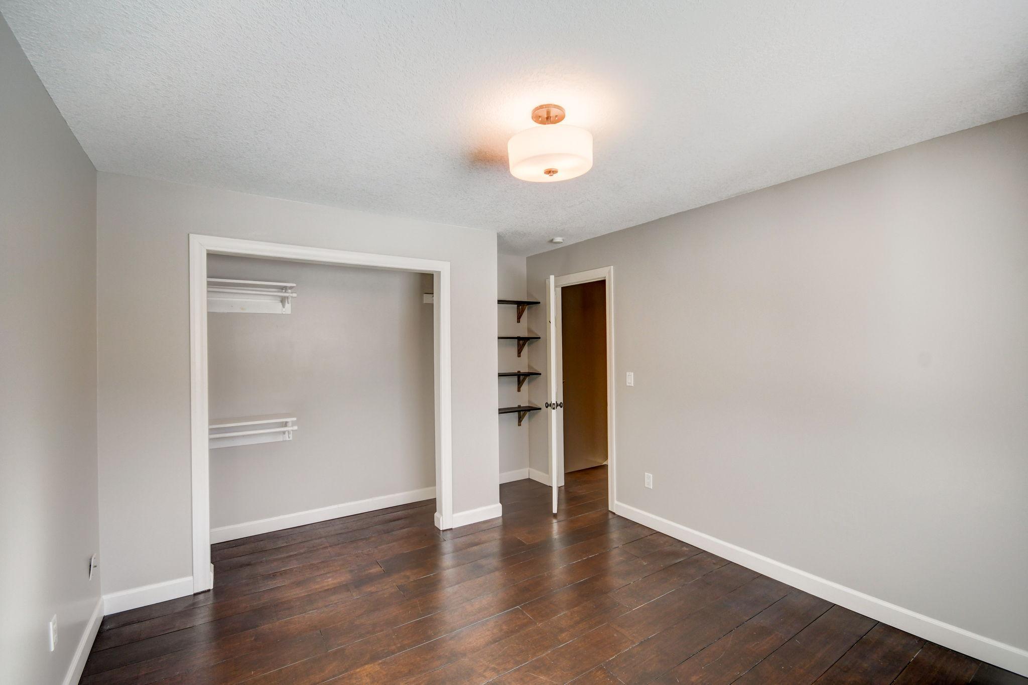 Empty bedroom with dark wood floors, an open closet, and built-in shelves.