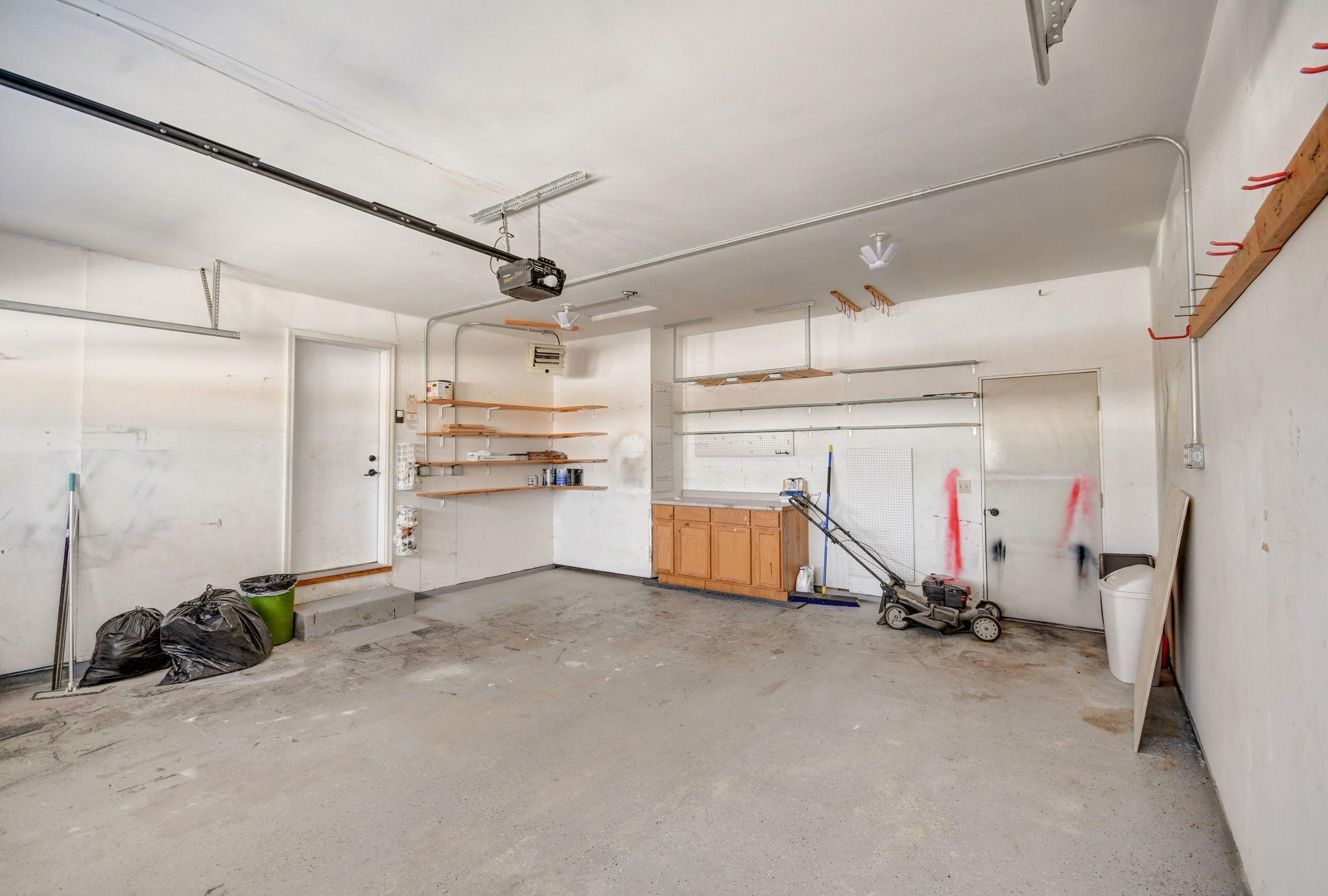 Garage with wall-mounted shelves, a wood-cabinet workbench, and a lawn mower.