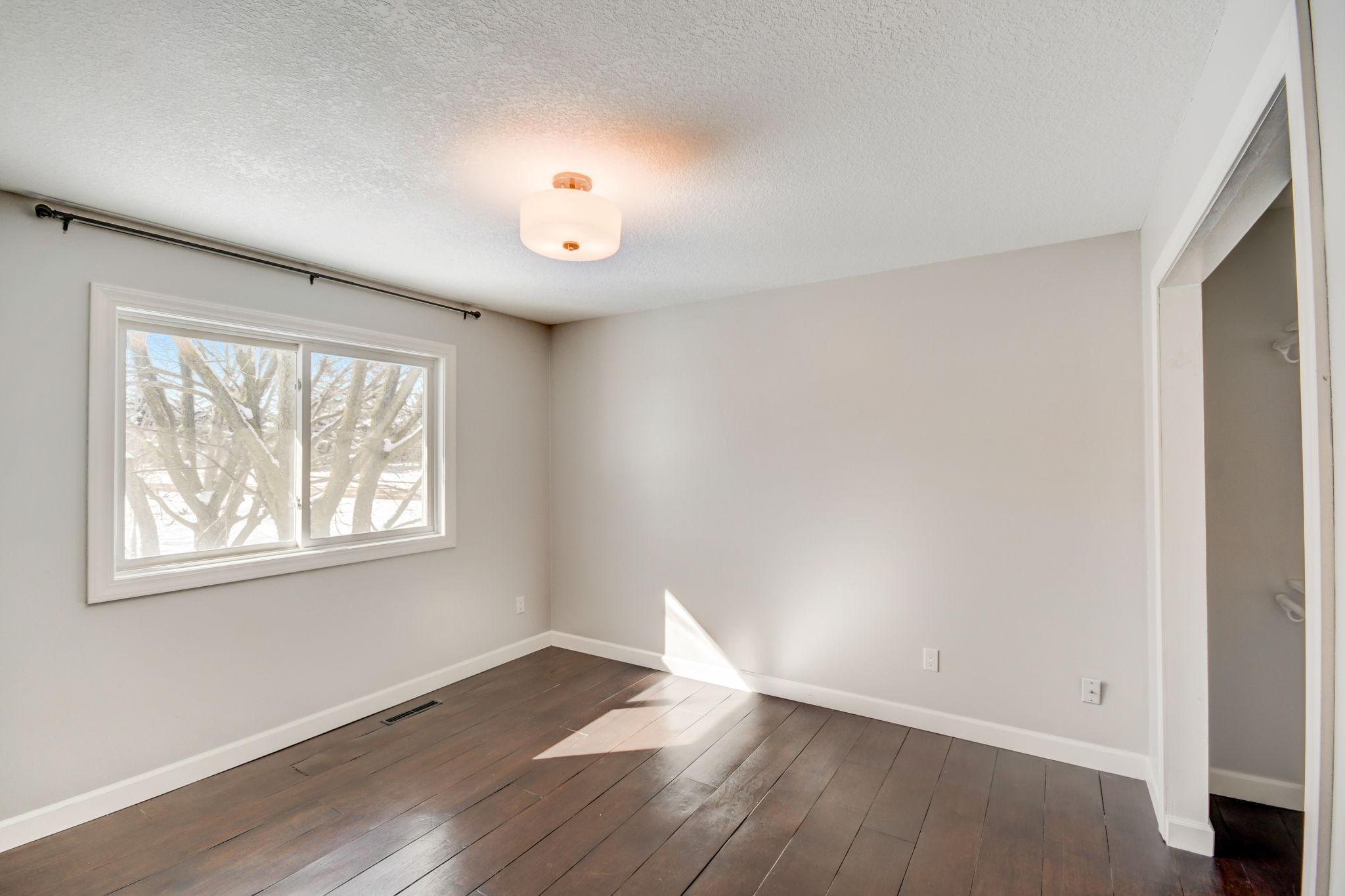 Empty bedroom with dark plank flooring and a large window overlooking snowy trees.
