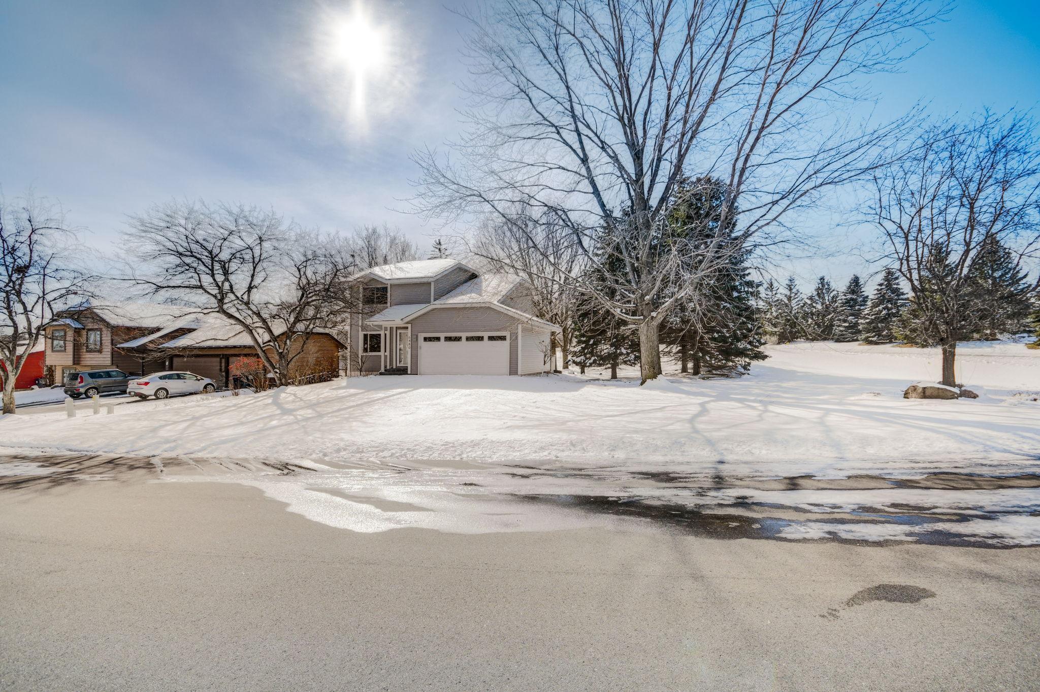 Two-story house with an attached garage amid snow-covered trees and yard.