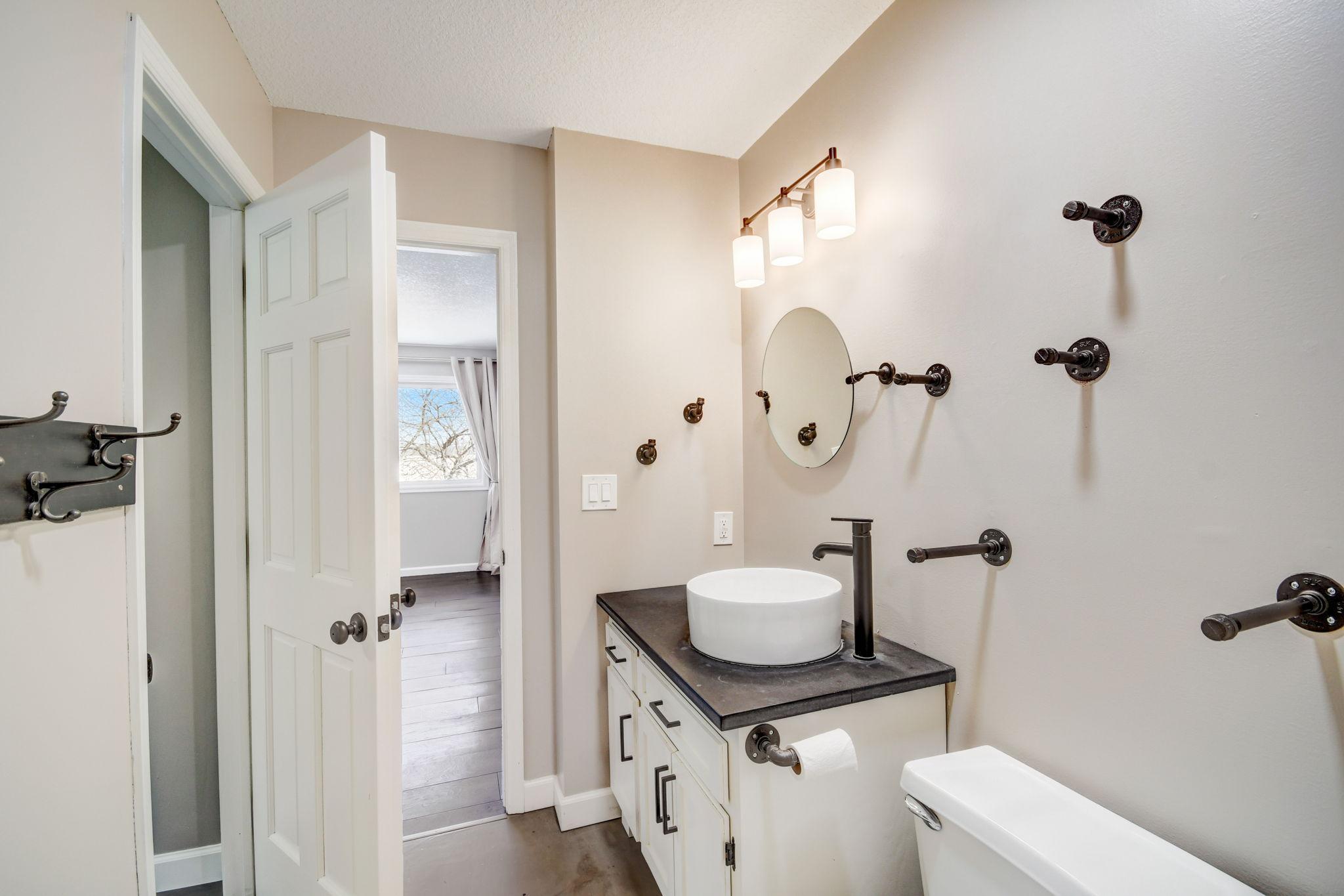 Bathroom with a white vessel sink, dark countertop, oval mirror, and bronze wall-mounted fixtures.