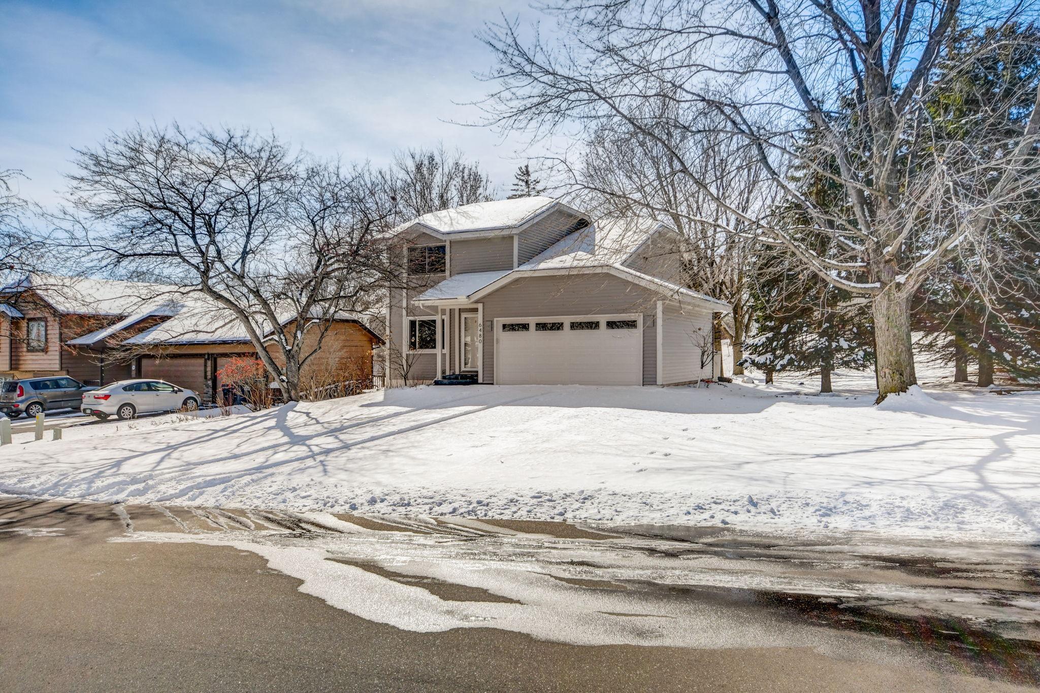 Gray two-story house with an attached garage, framed by bare trees above a snow-covered yard.