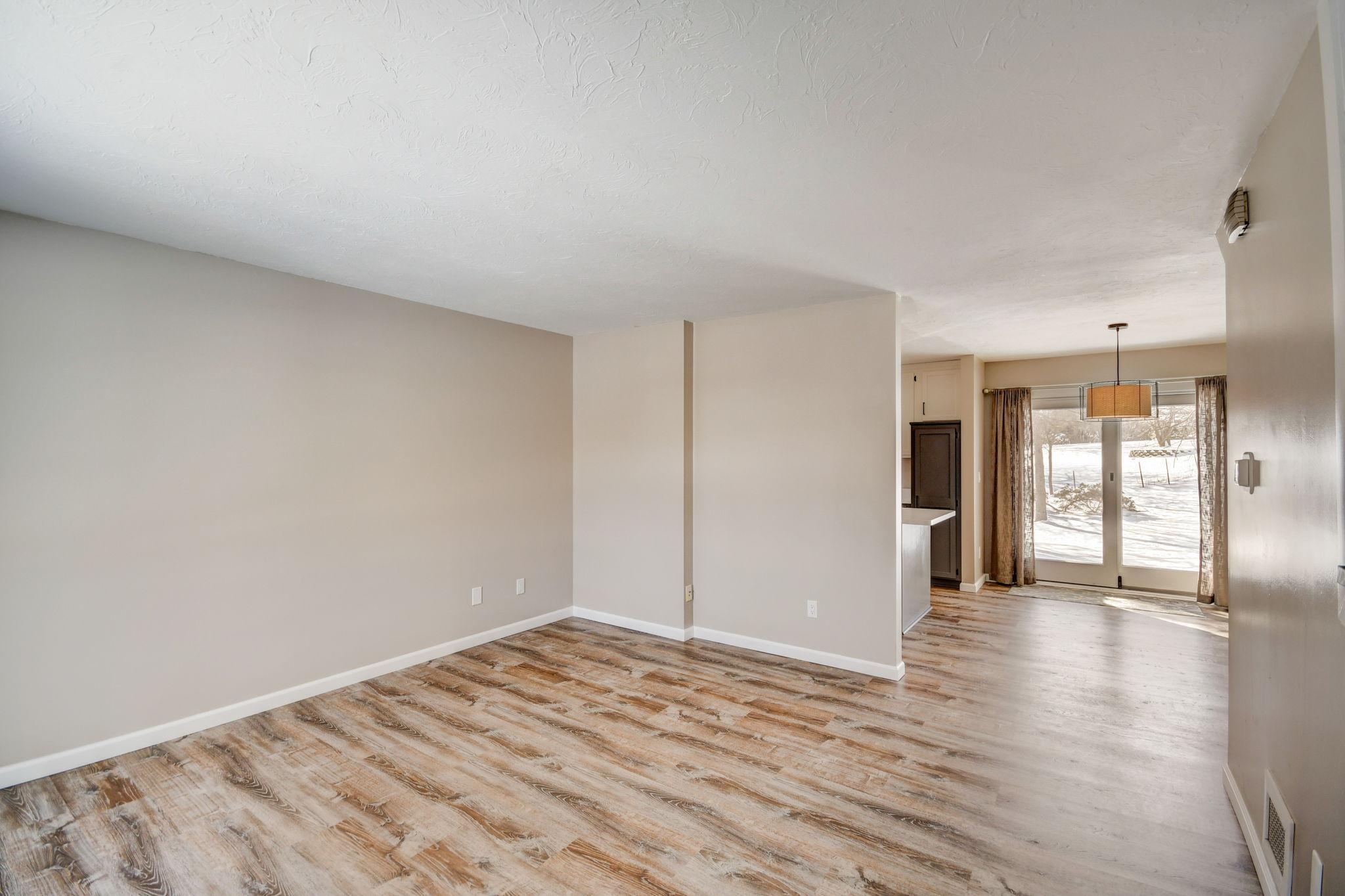 Empty living and dining area with wood-look floors and sliding glass doors overlooking a snowy yard.