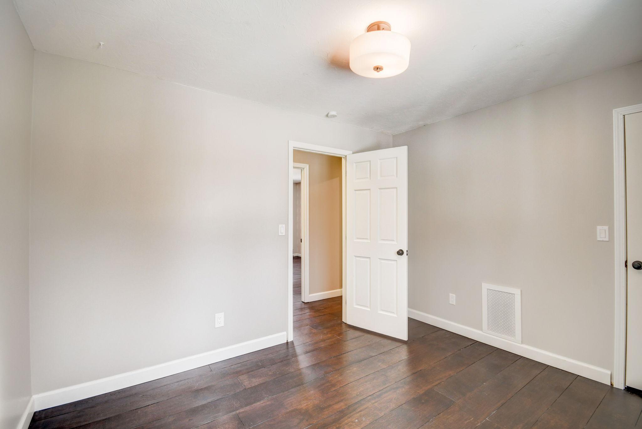 Unfurnished room with dark hardwood floors, gray walls, and an open door to the hallway.