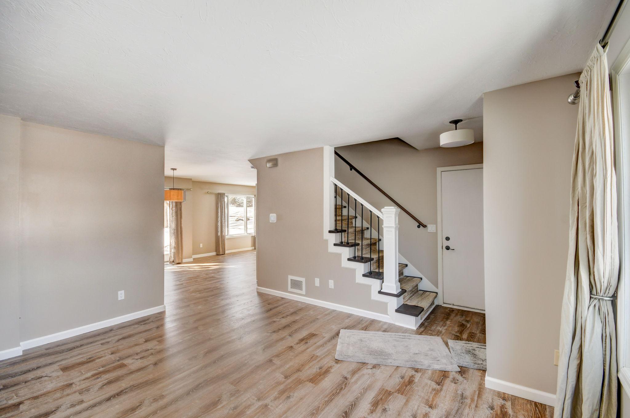 Mostly empty interior with wood-look floors, a staircase, and a sunlit adjoining room.