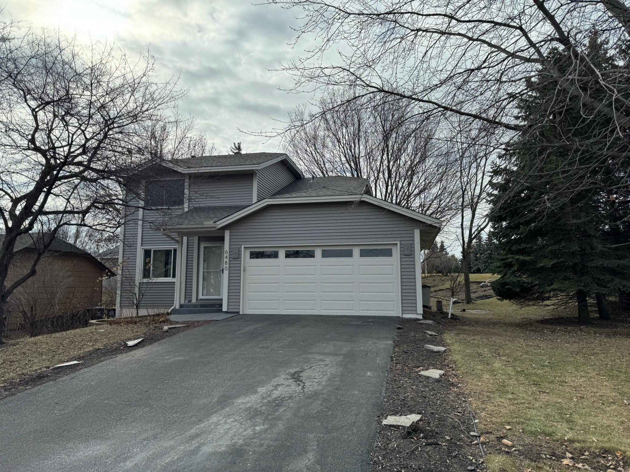 Two-story gray house with a white double garage door and paved driveway.
