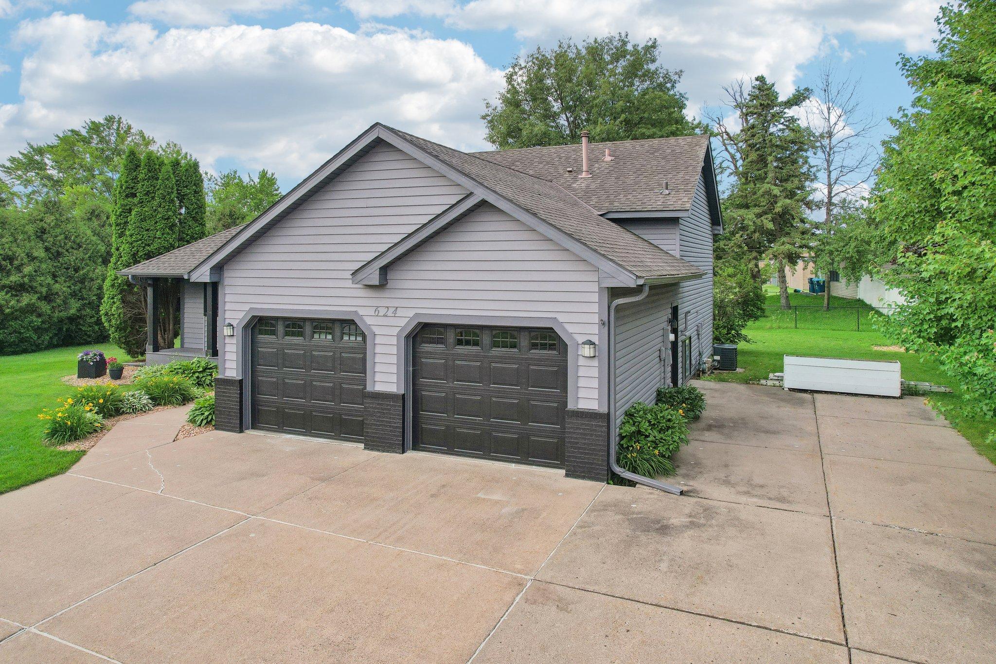 Gray-sided home with two dark garage doors, a wide concrete driveway, and landscaped beds.