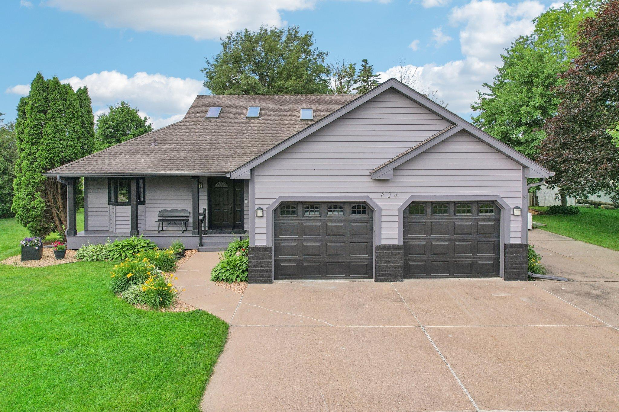 Gray-sided house with two garage doors, a covered porch, roof skylights, and landscaped front lawn.