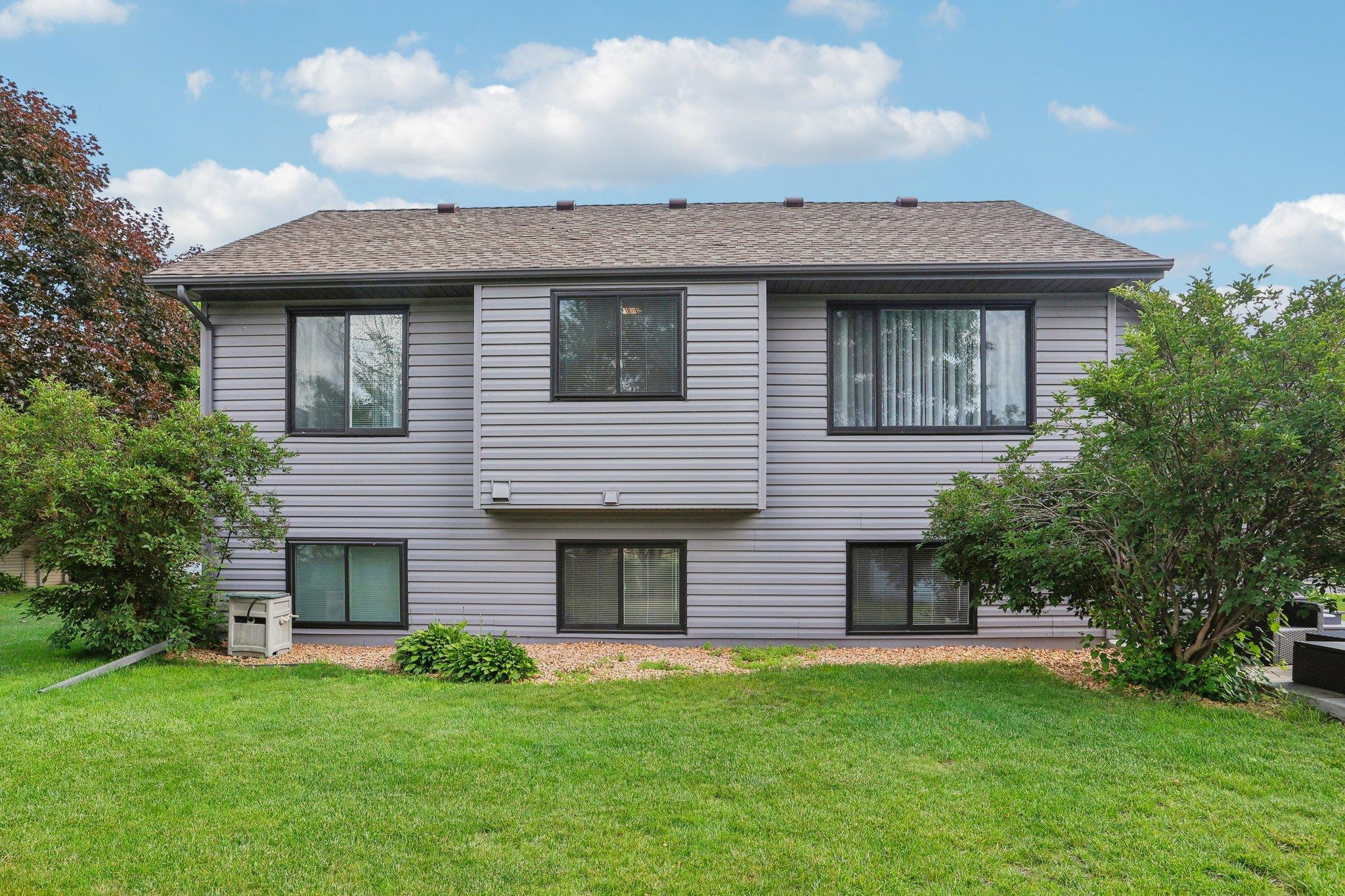 Rear exterior of a gray-sided two-story home with dark-framed windows and a shrub-lined lawn.