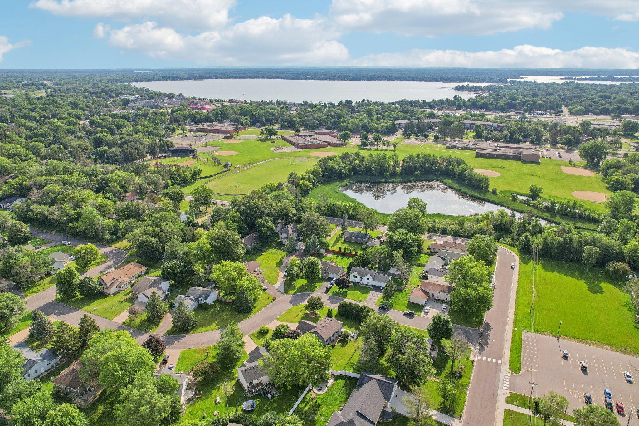 Aerial view of a leafy neighborhood with a pond, baseball fields, and a lake in the distance.