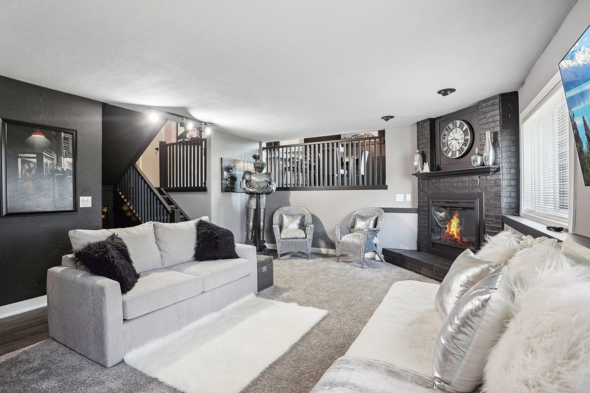 Living room with a lit brick fireplace, staircase, and loft railing behind light-colored sofas.