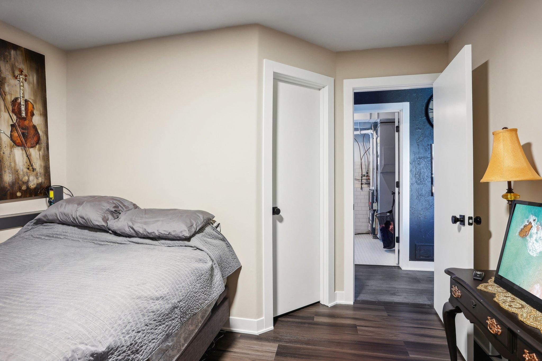 Bedroom with a gray quilted bed, violin artwork, and an open doorway to a utility area.