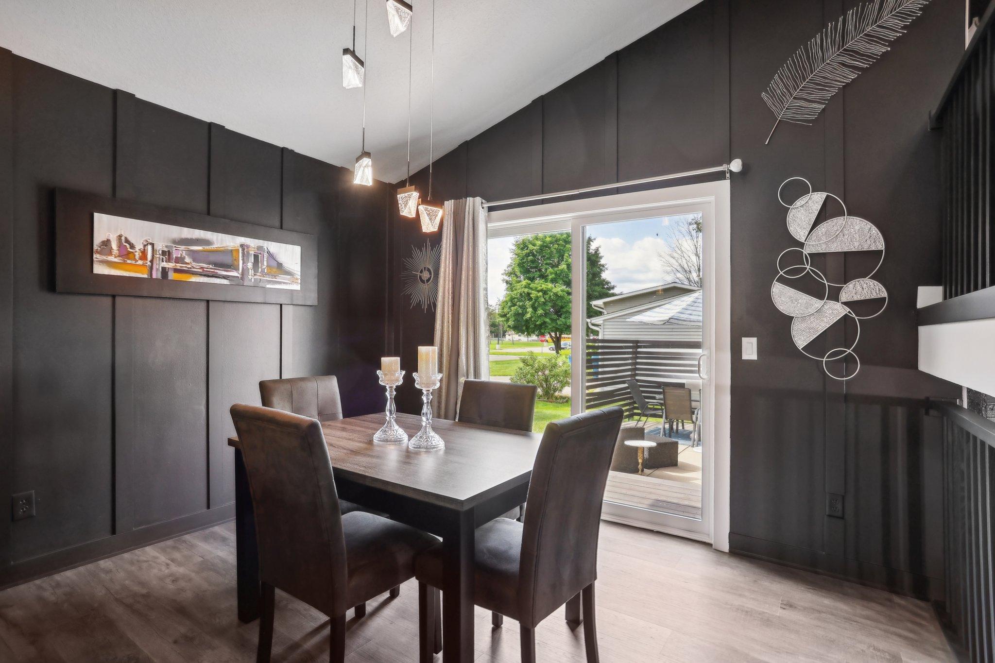 Dining room with charcoal paneled walls, dark furnishings, pendant lights, and a sliding glass door to the deck.