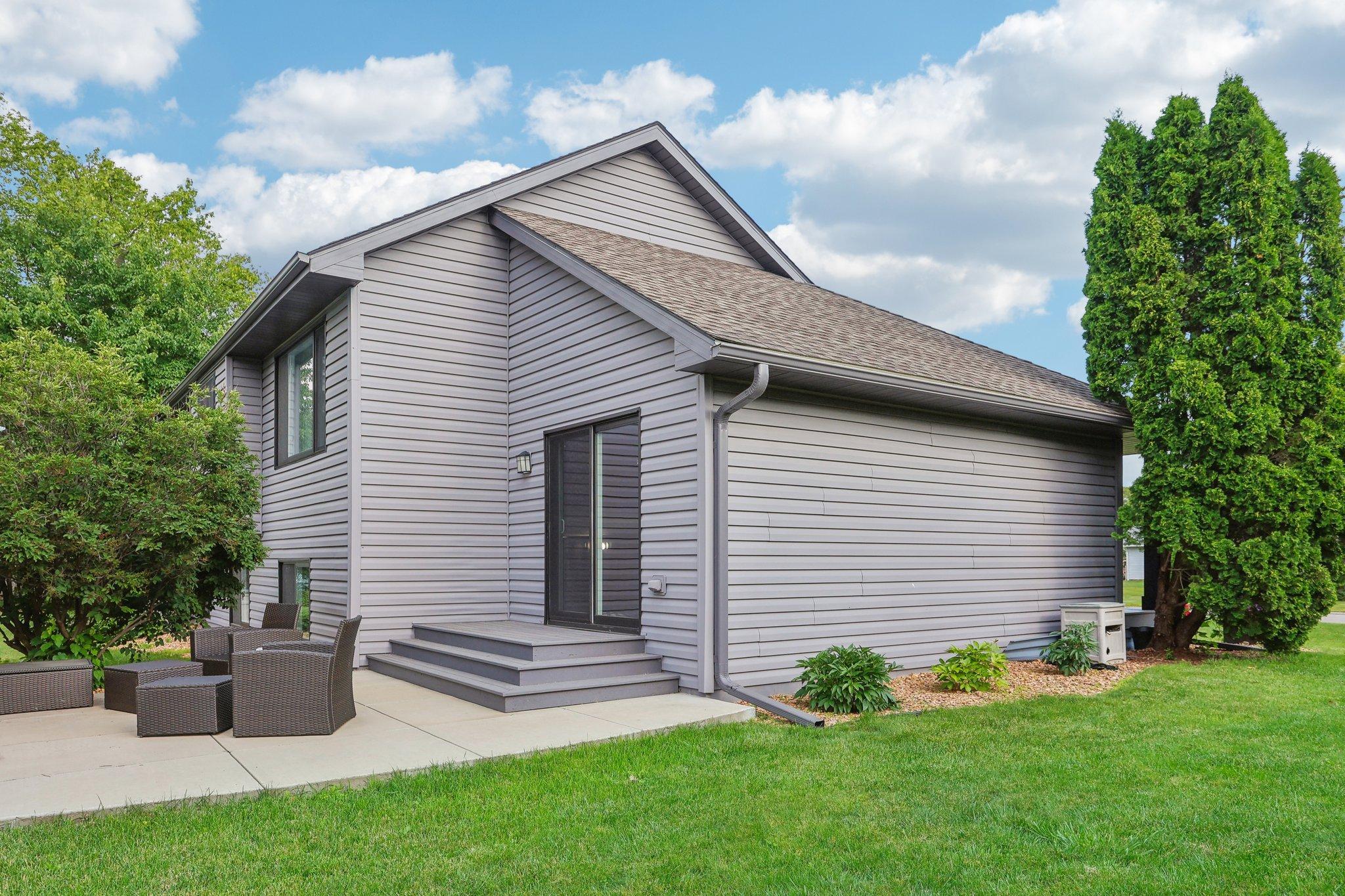 Gray-sided house with a sliding patio door opening onto a concrete patio with wicker seating.