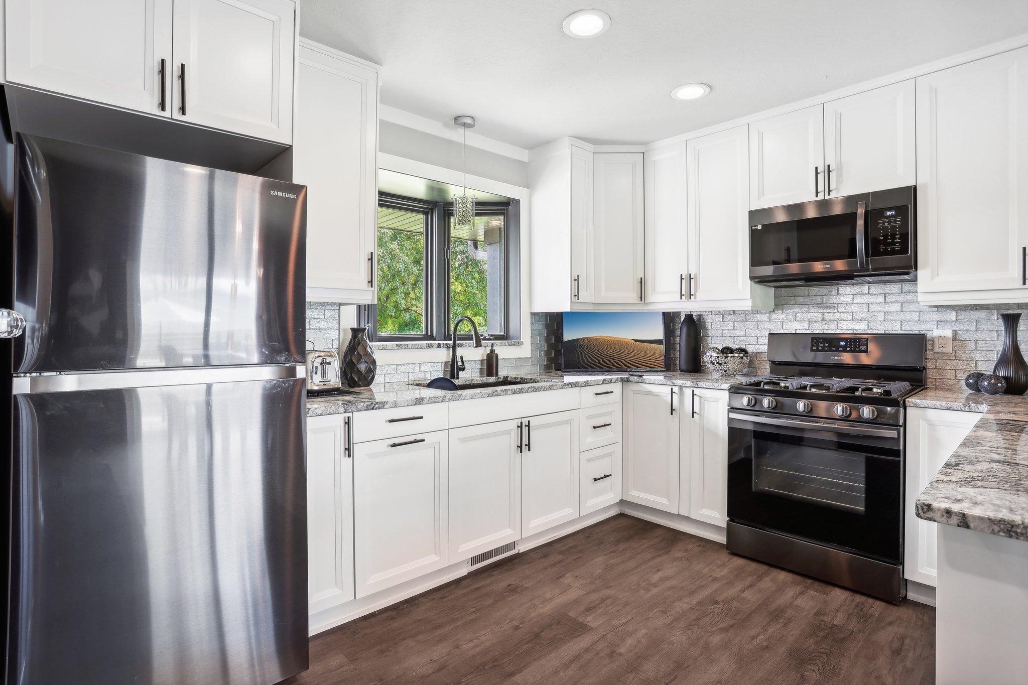 Bright white kitchen with granite counters, stainless appliances, and a window above the sink.