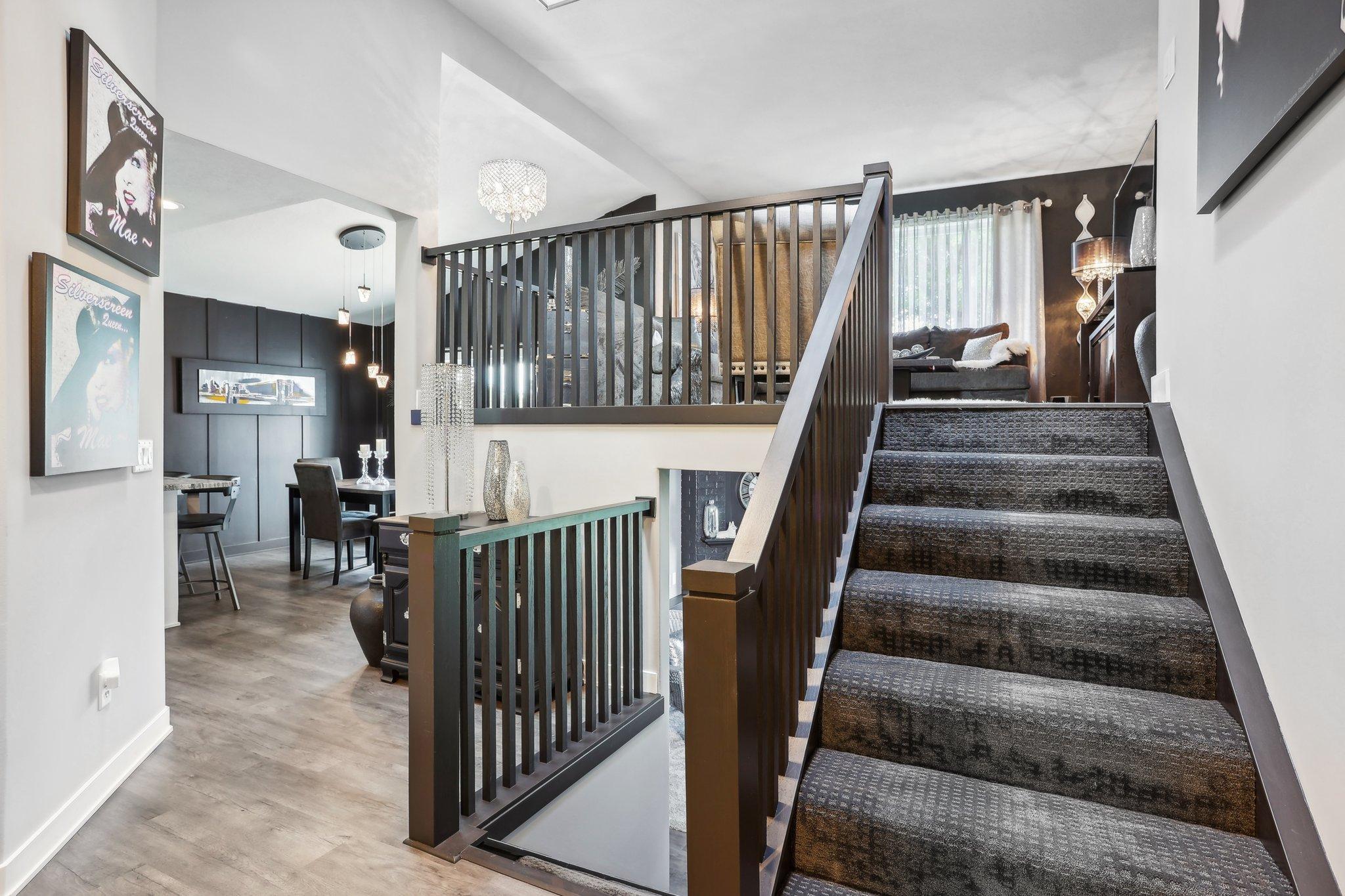 Furnished stair landing with dark railings, carpeted stairs, and a dining area below.
