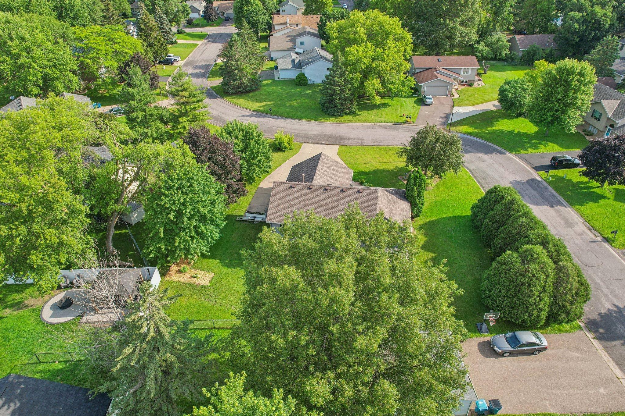 Aerial view of a tree-shaded home with a fenced yard and circular patio.