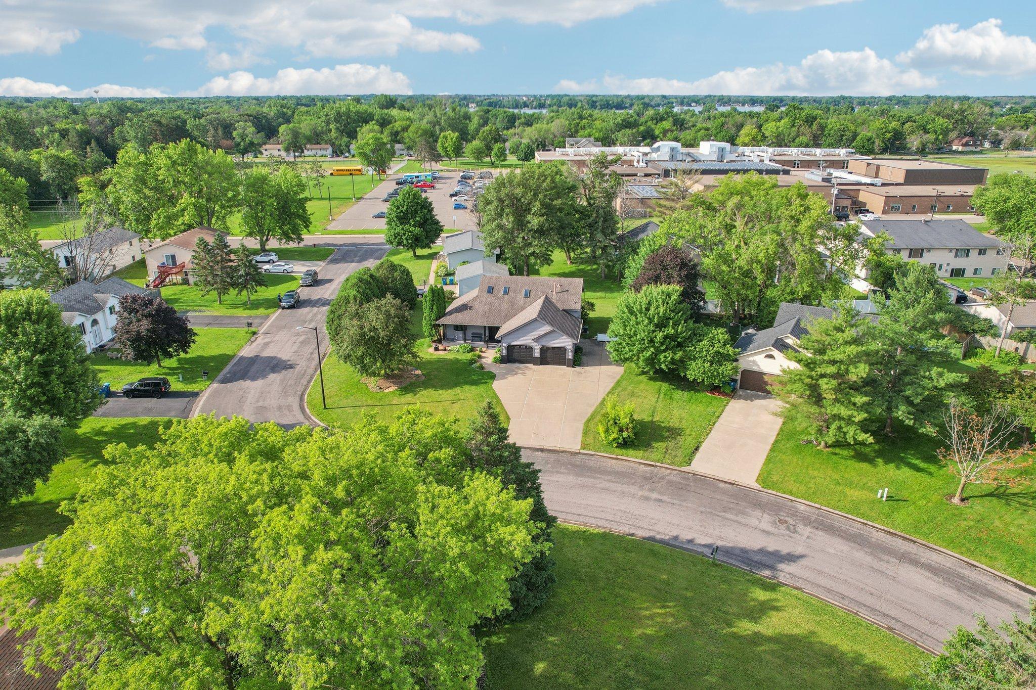 Aerial view of a suburban home with a two-car garage, broad driveway, and leafy trees.