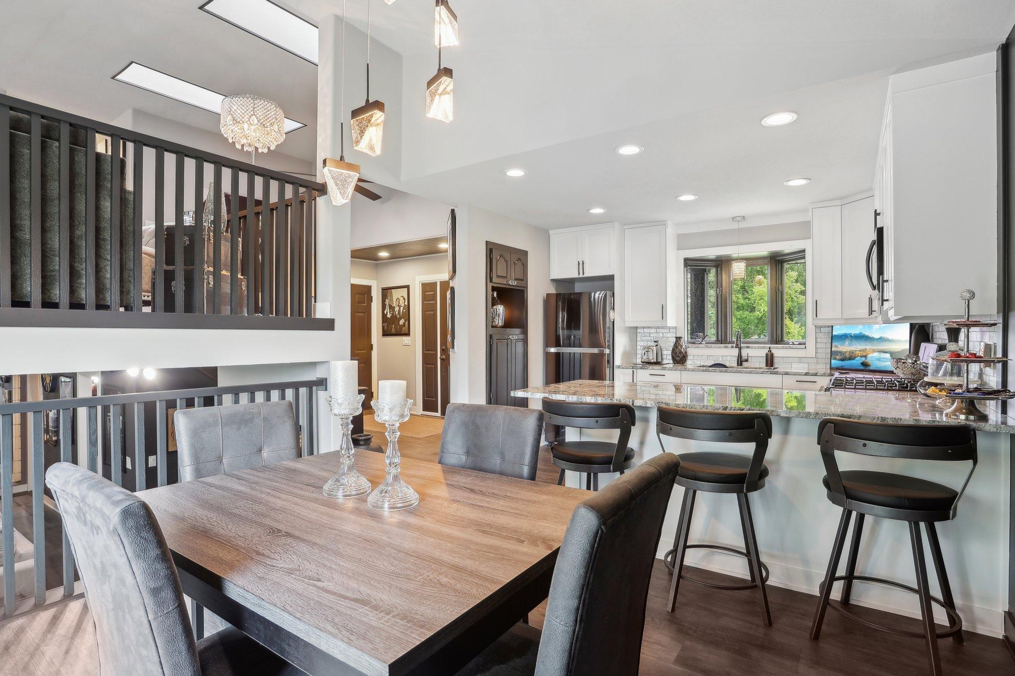 Open-plan dining area and kitchen with a wood table, granite breakfast bar, and white cabinetry.