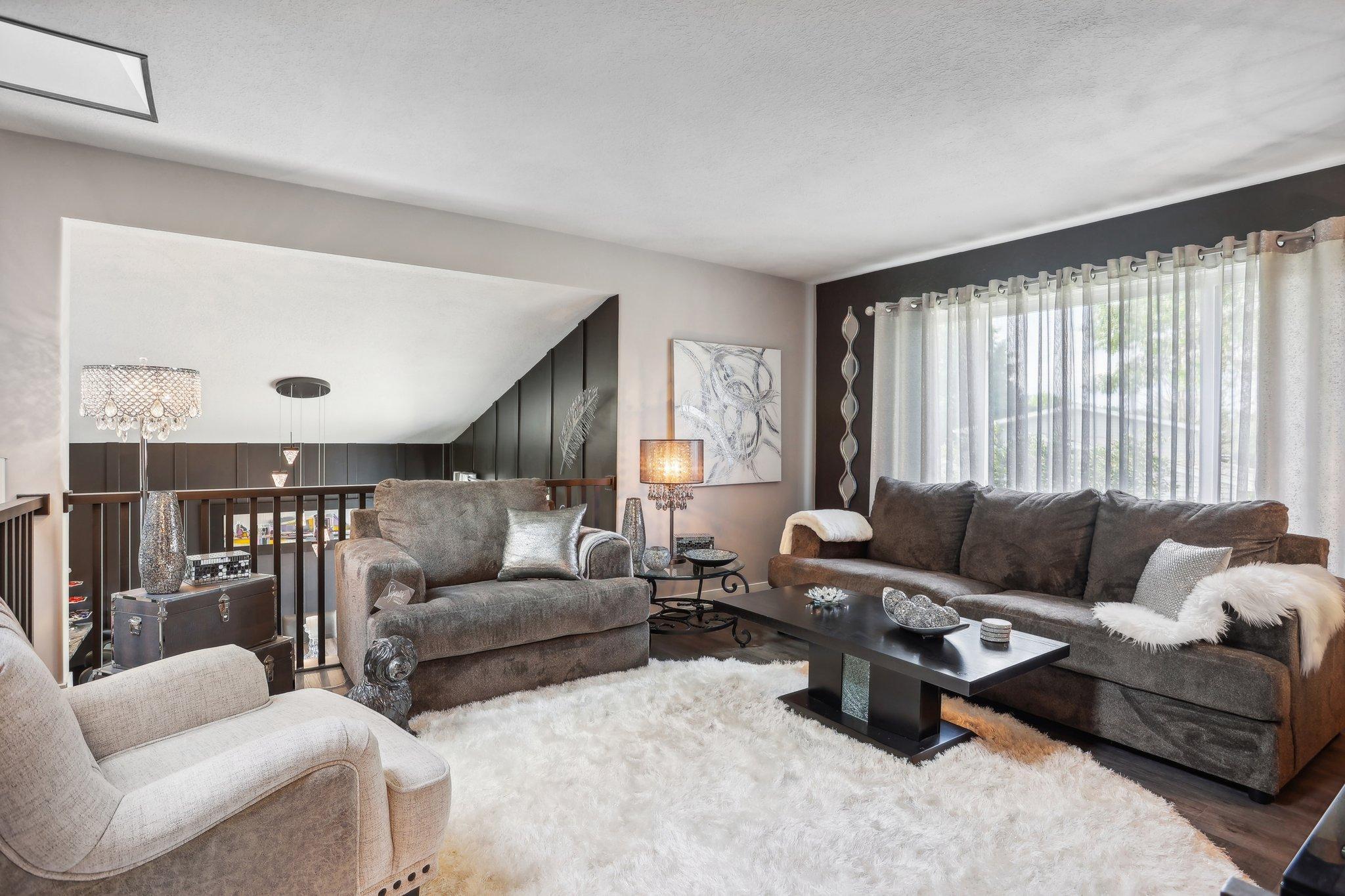 Living room with gray sofas, a white shag rug, and a railing overlooking an open level.