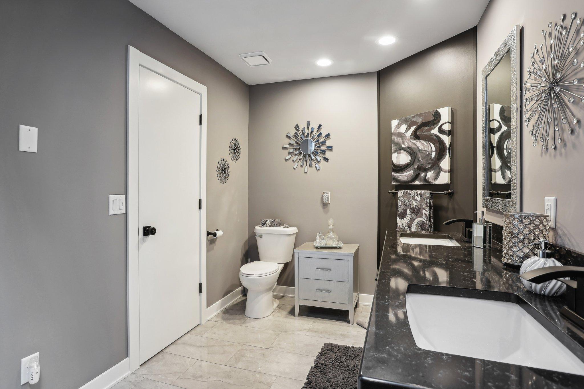 Bathroom with a dark granite double vanity, two sinks, and a toilet.