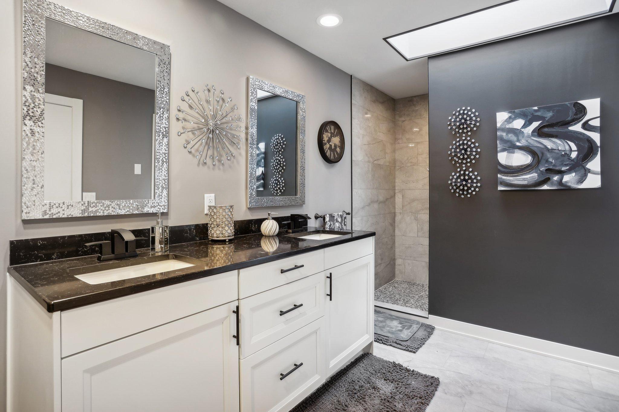 Modern bathroom with a white vanity, dark countertop, framed mirrors, and tiled walk-in shower.
