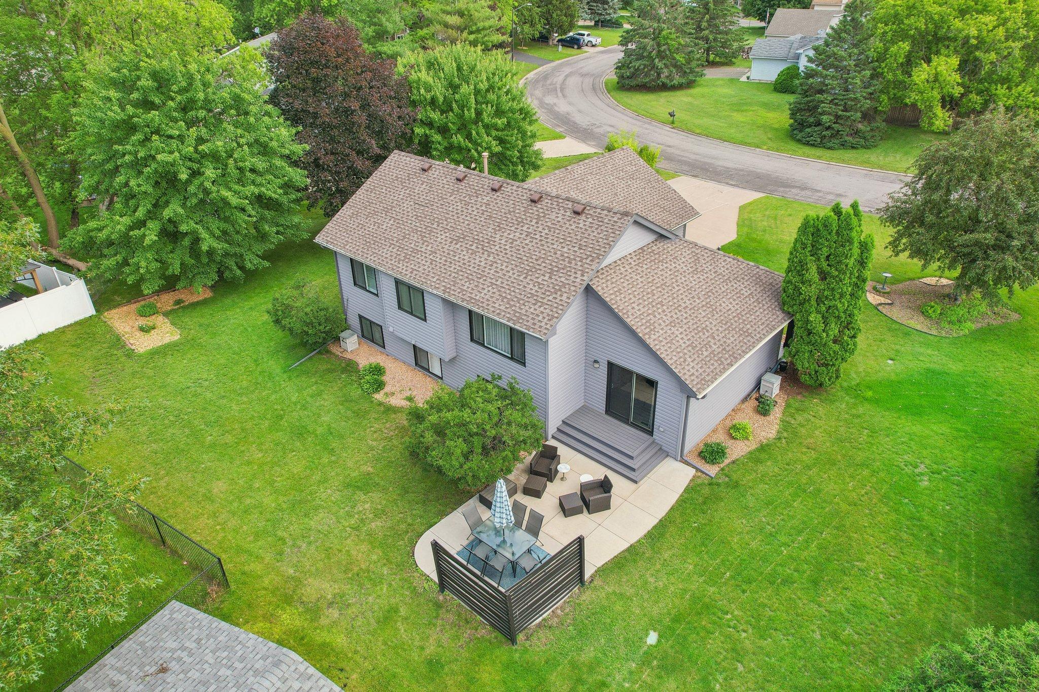 Aerial view of a gray house, spacious lawn, and patio with outdoor dining furniture.