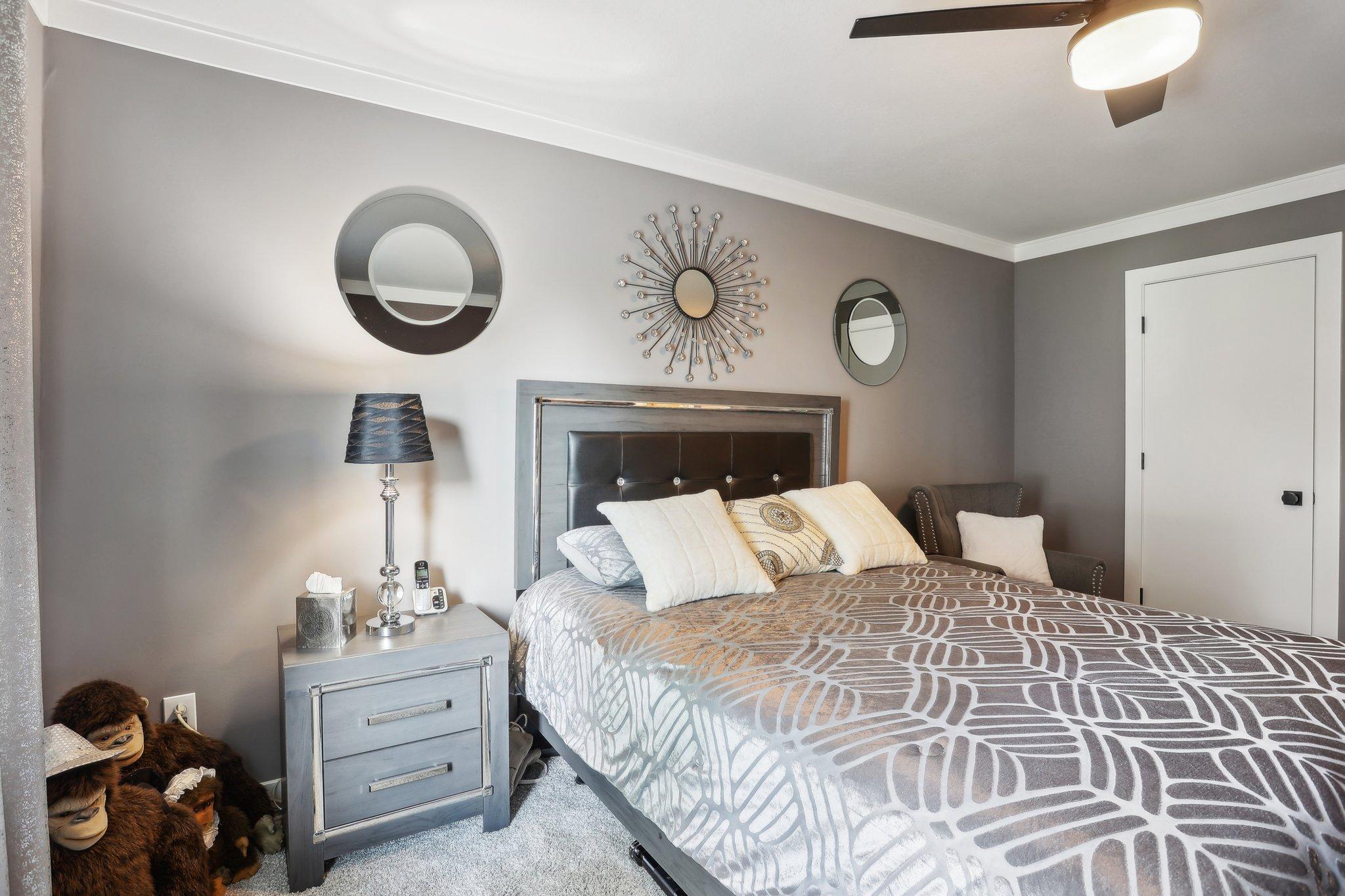 Furnished bedroom with geometric gray bedding, a dark headboard, decorative mirrors, and stuffed toys.