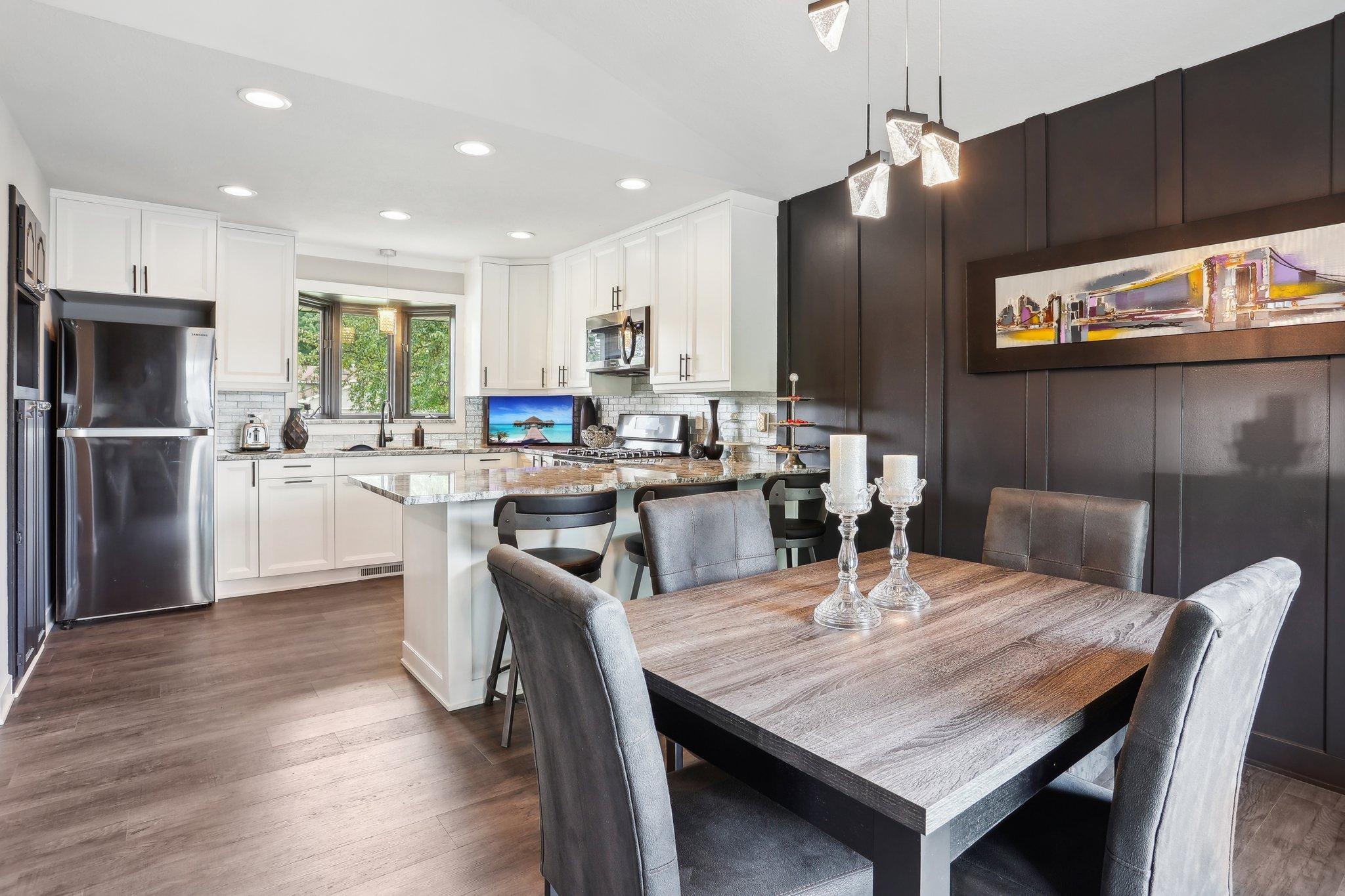 Kitchen and dining area with a granite island, white cabinetry, and a wood table against a dark accent wall.