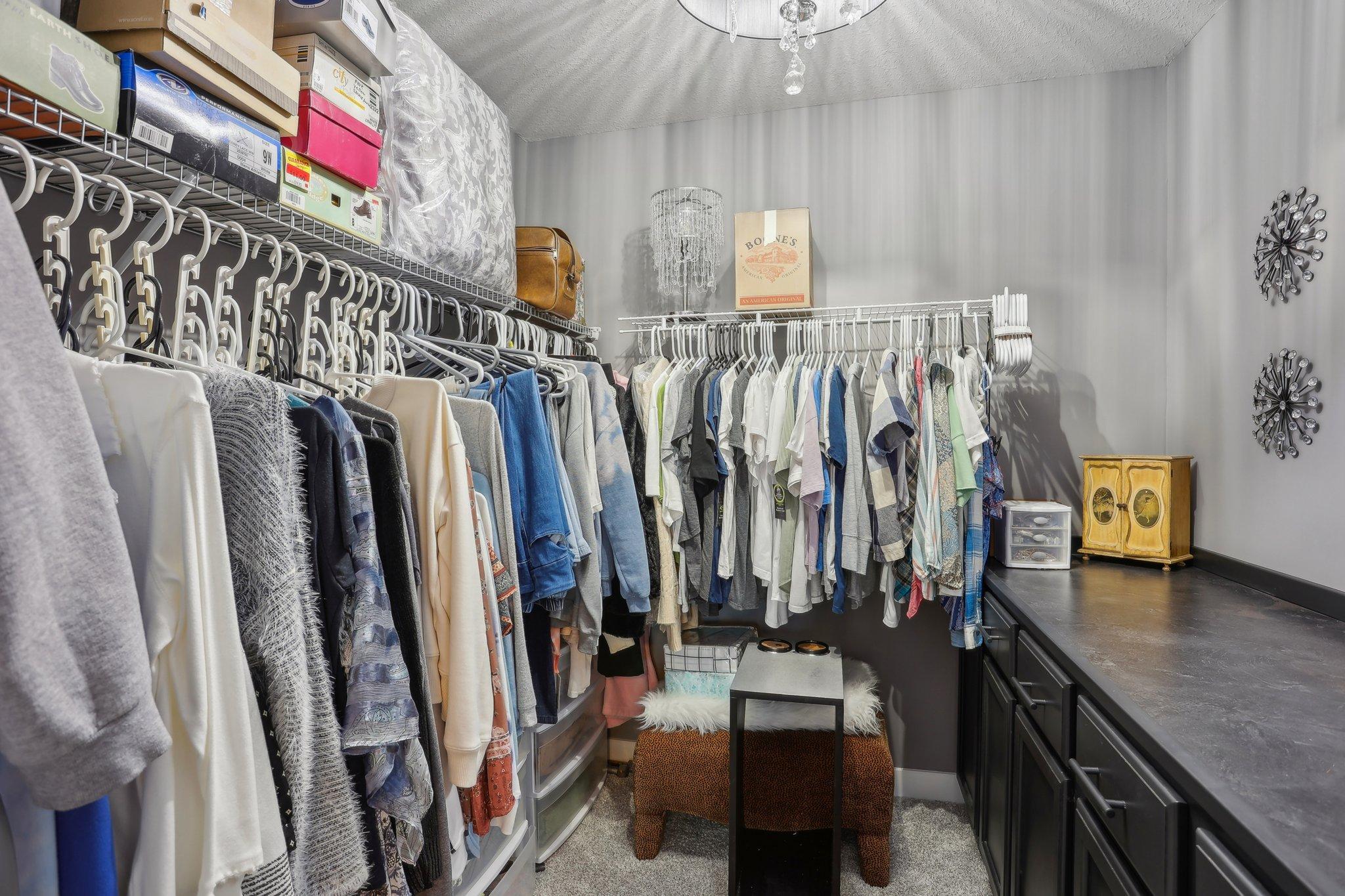 Walk-in closet with extensive clothing racks, dark cabinetry, and a small upholstered seat.