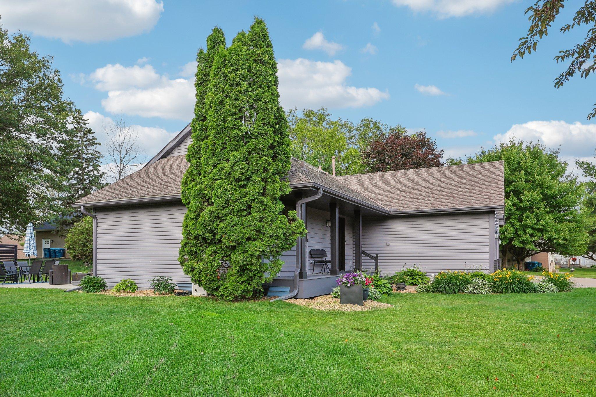 Gray-sided home with a covered patio, flower beds, and a broad green lawn.