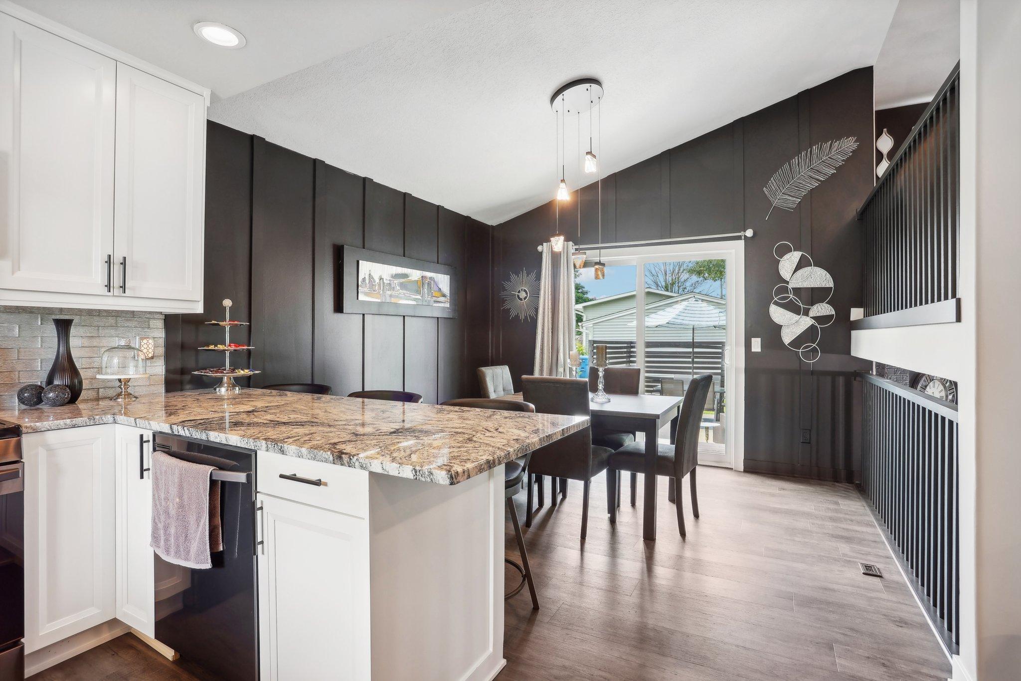 Kitchen and dining area with a large stone island, dark paneled walls, and sliding doors to the patio.