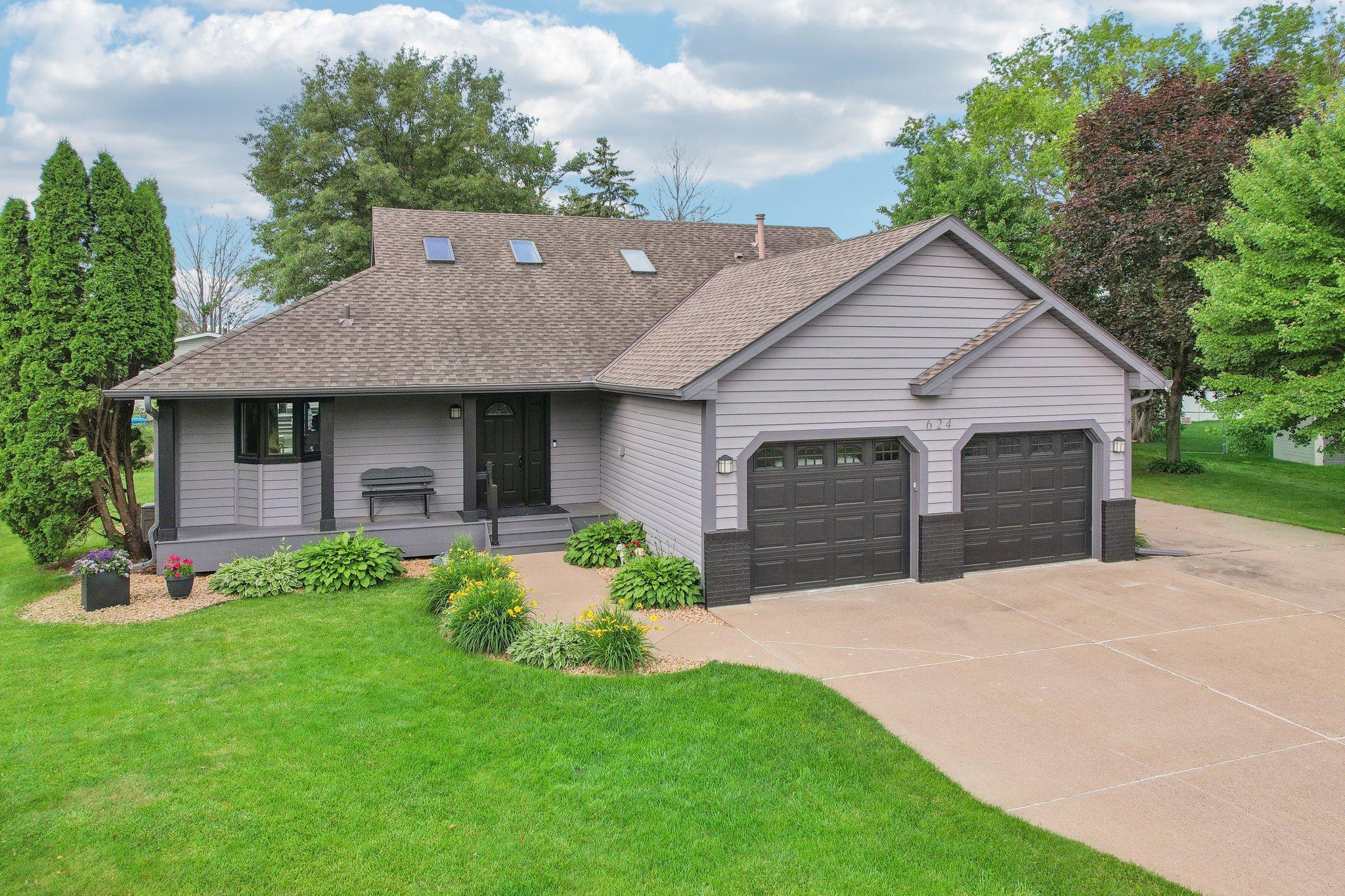 Gray-sided house with a covered porch, double garage, skylights, and landscaped front lawn.