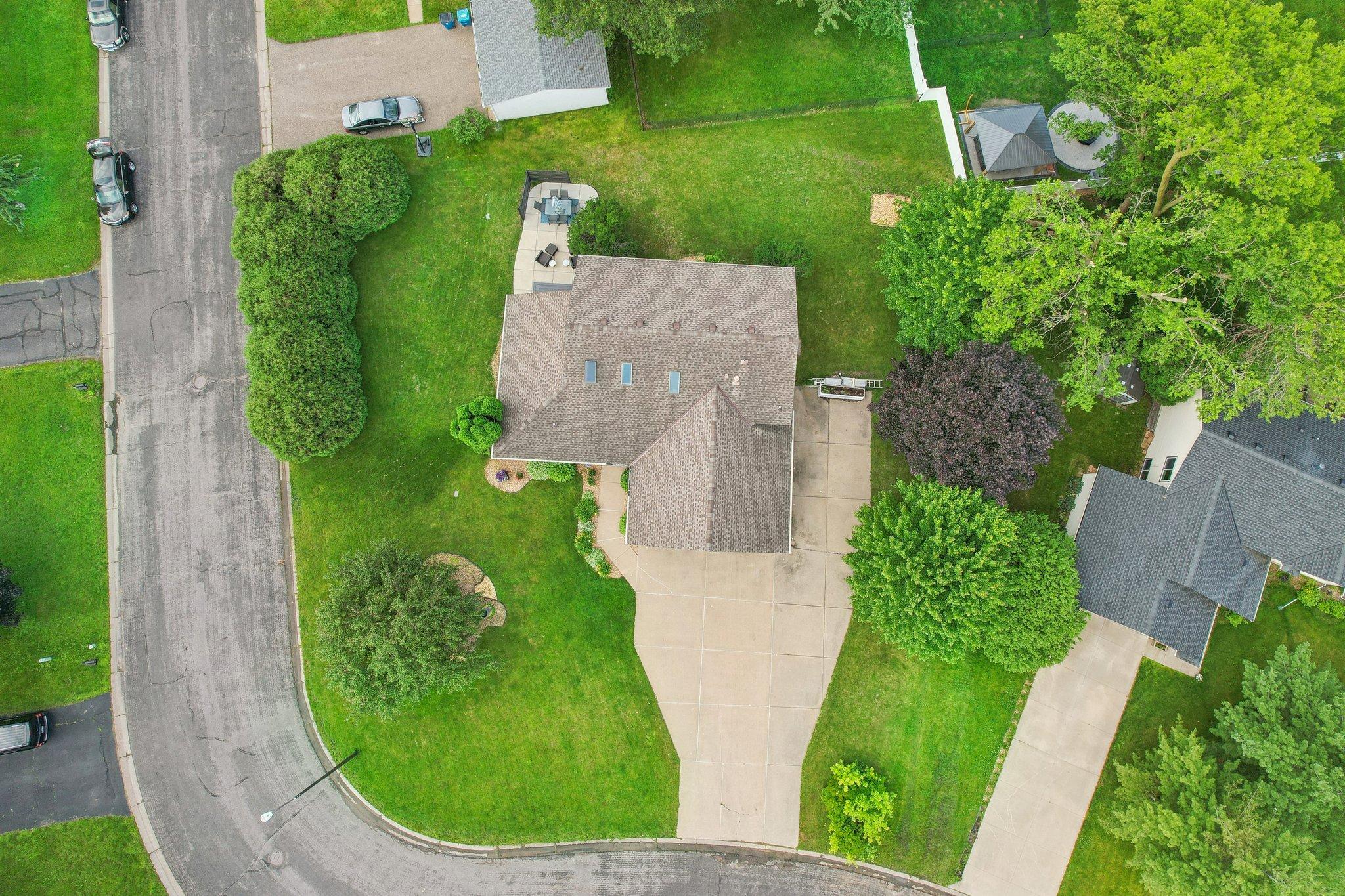Aerial view of a home with a broad driveway, landscaped lawn, mature trees, and a backyard patio.