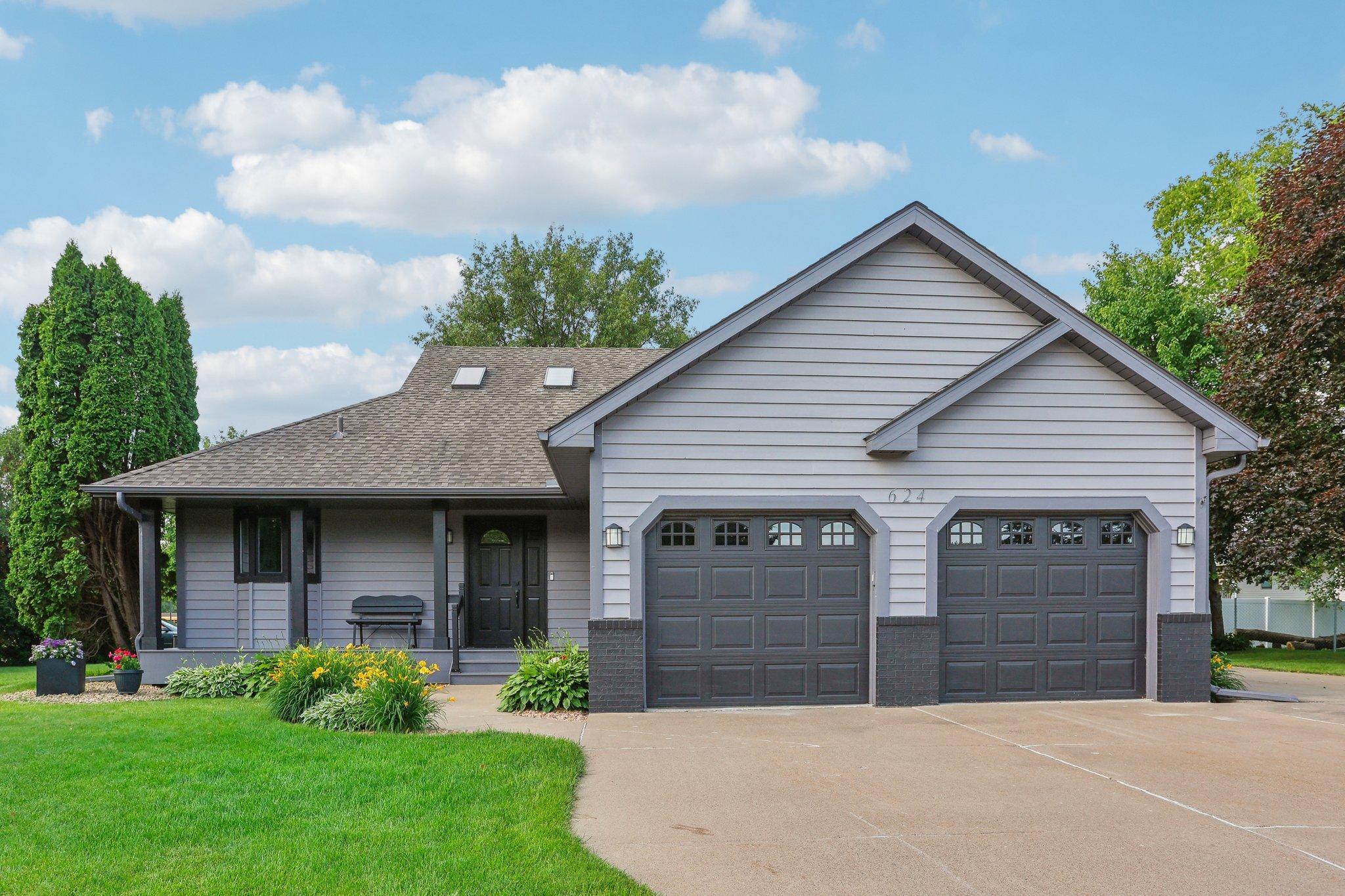 Gray-sided house with two dark garage doors, skylights, and a landscaped front lawn.