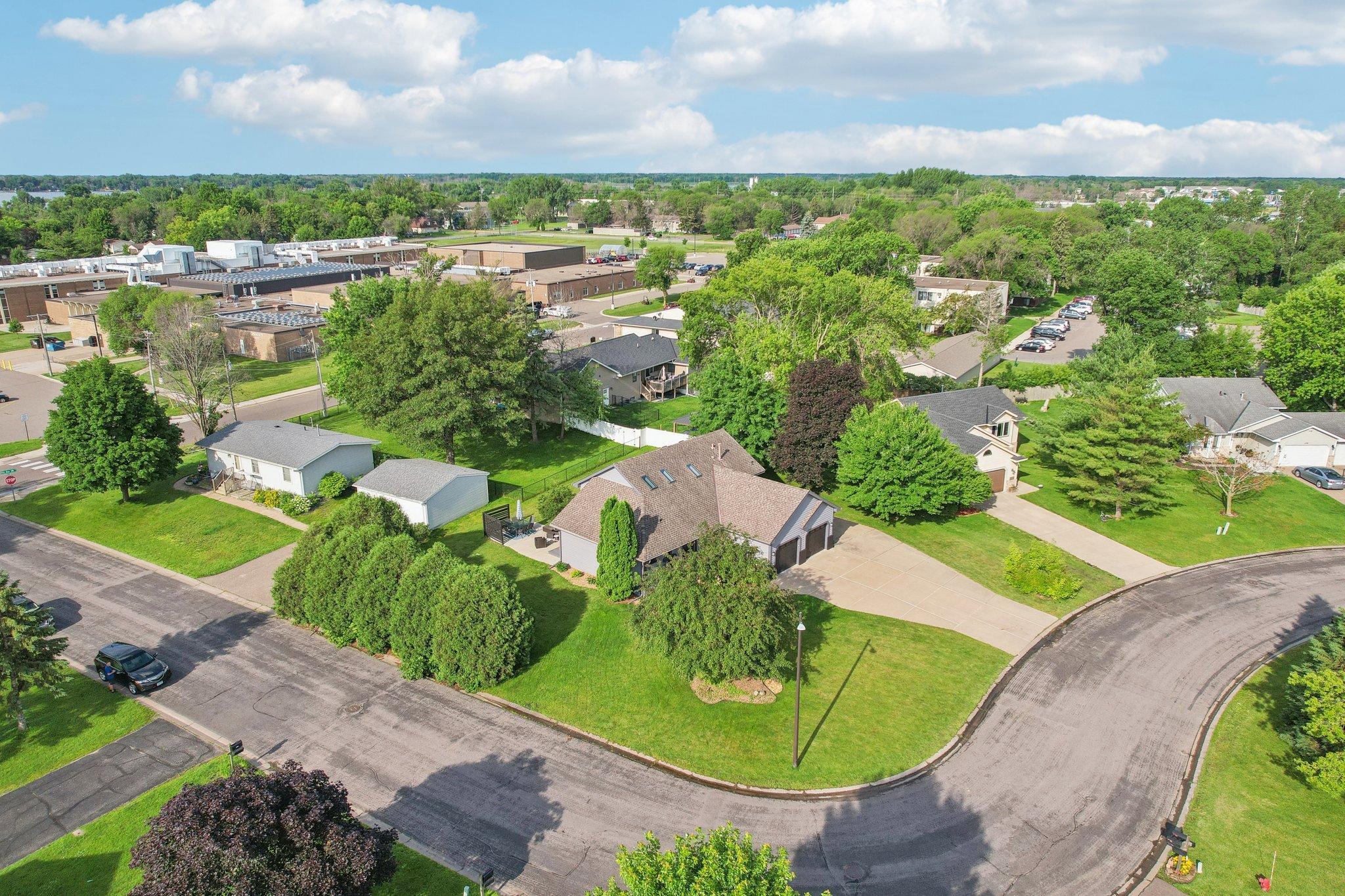 Aerial view of a tan-roofed house with an attached garage, broad lawn, and mature trees.
