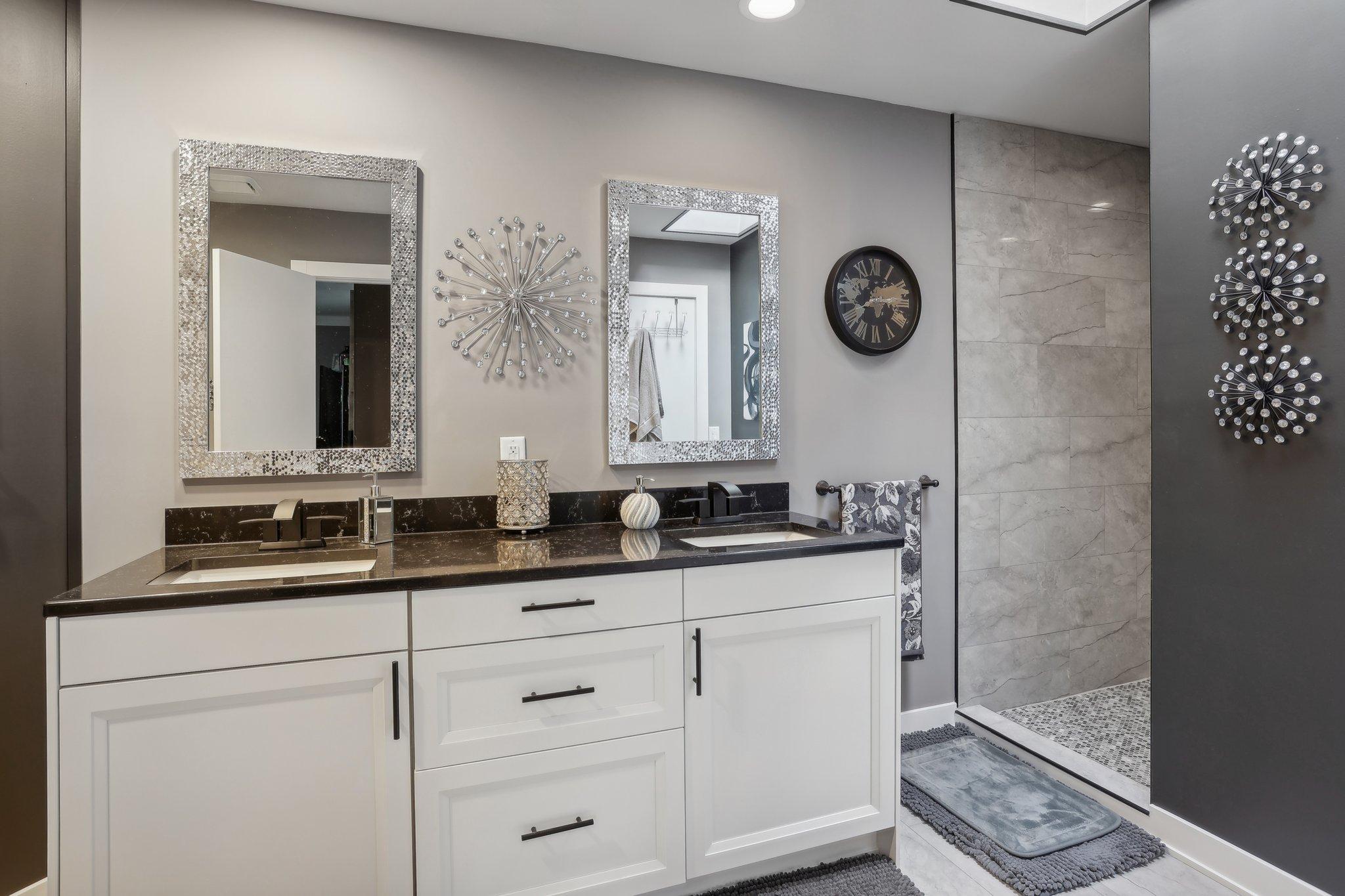 Bathroom with a white double vanity and dark countertop beside a tiled walk-in shower.