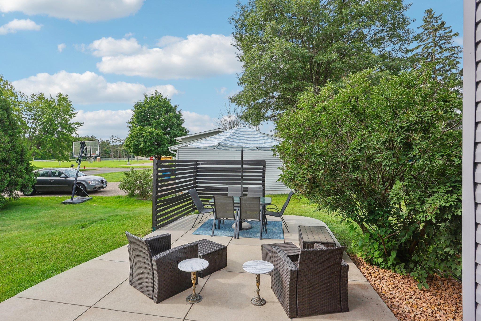 Furnished backyard patio with wicker seating, a striped umbrella, and a dark slatted privacy screen.