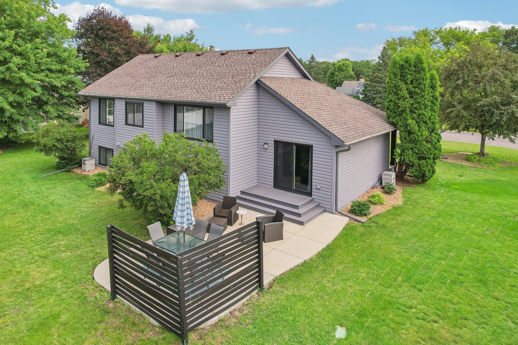 Rear of a gray-sided home with a fenced patio, outdoor seating, and a spacious green lawn.