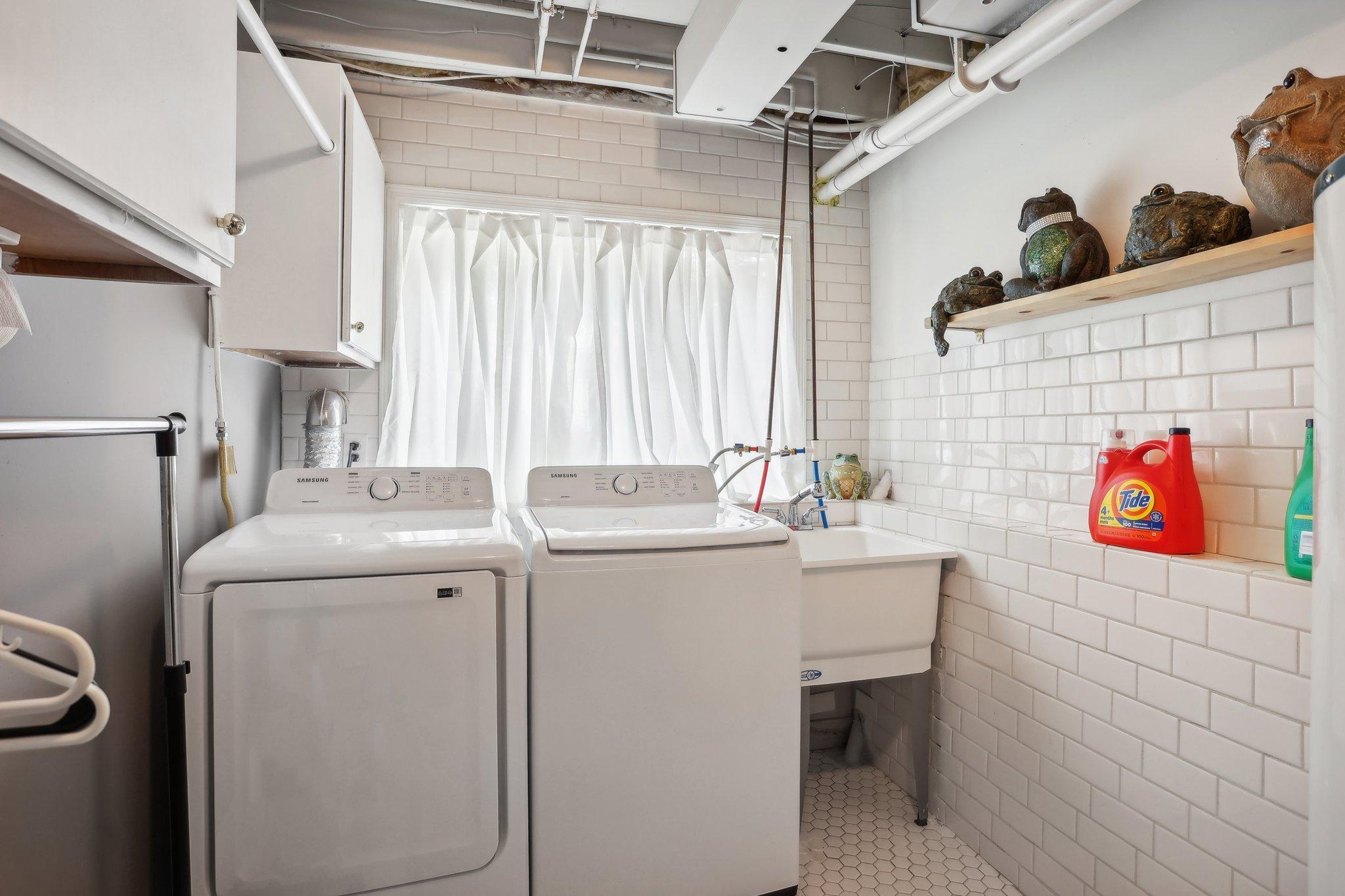 Laundry room with two white machines, a utility sink, and frog figurines on a shelf.