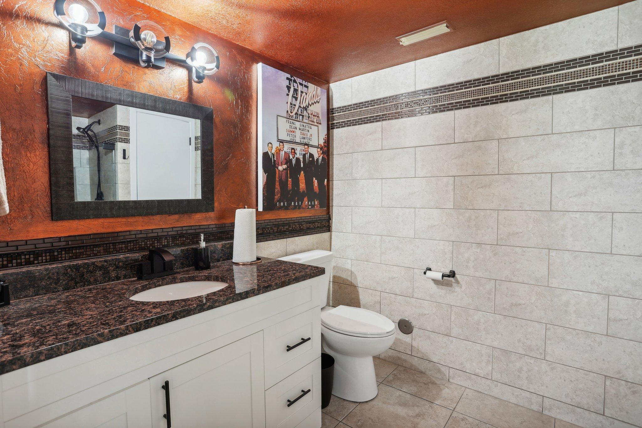 Bathroom with a white vanity, dark granite countertop, and light tiled walls with a mosaic border.