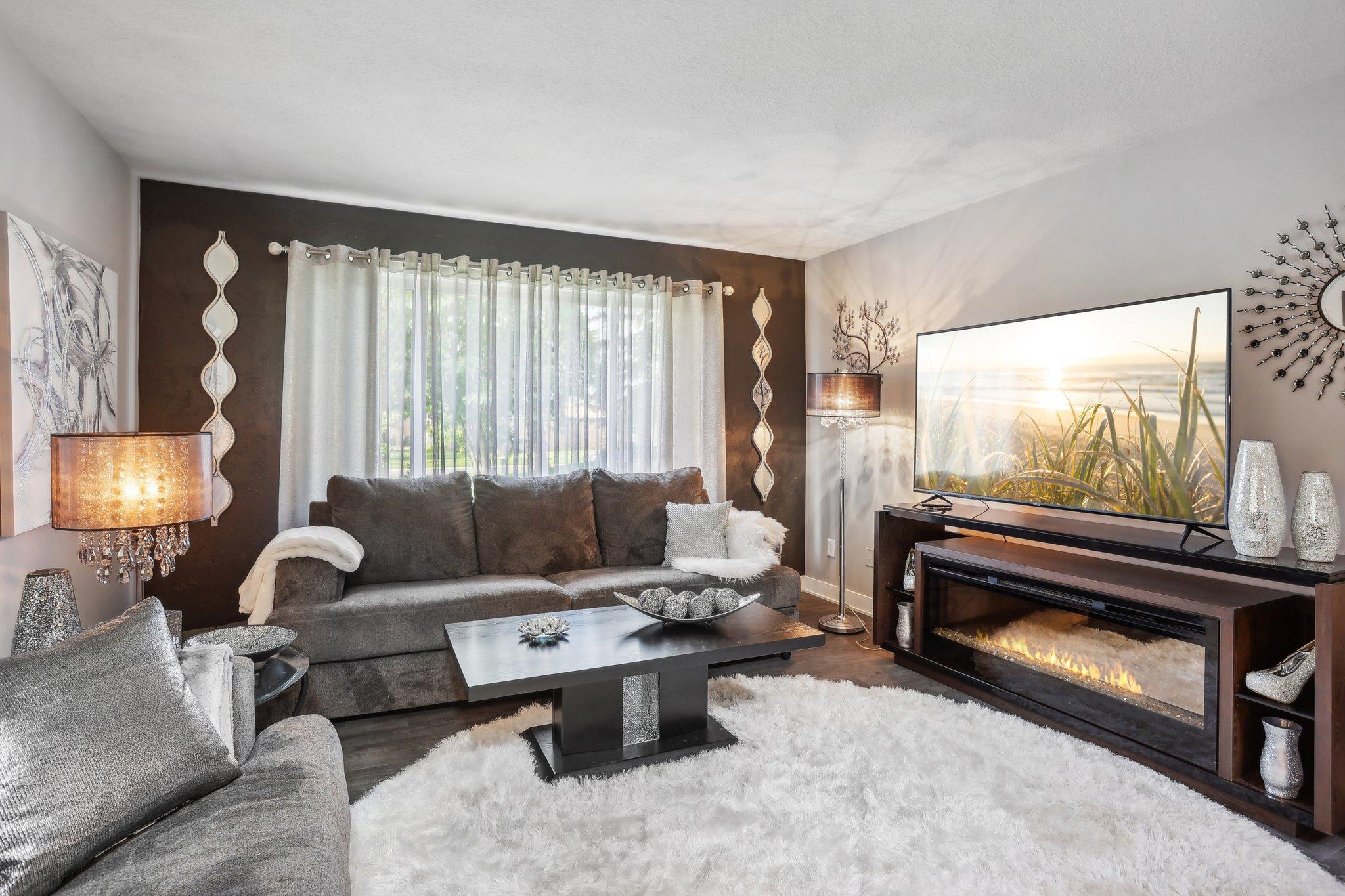 Living room with a gray sectional, electric fireplace, television, and plush white rug.